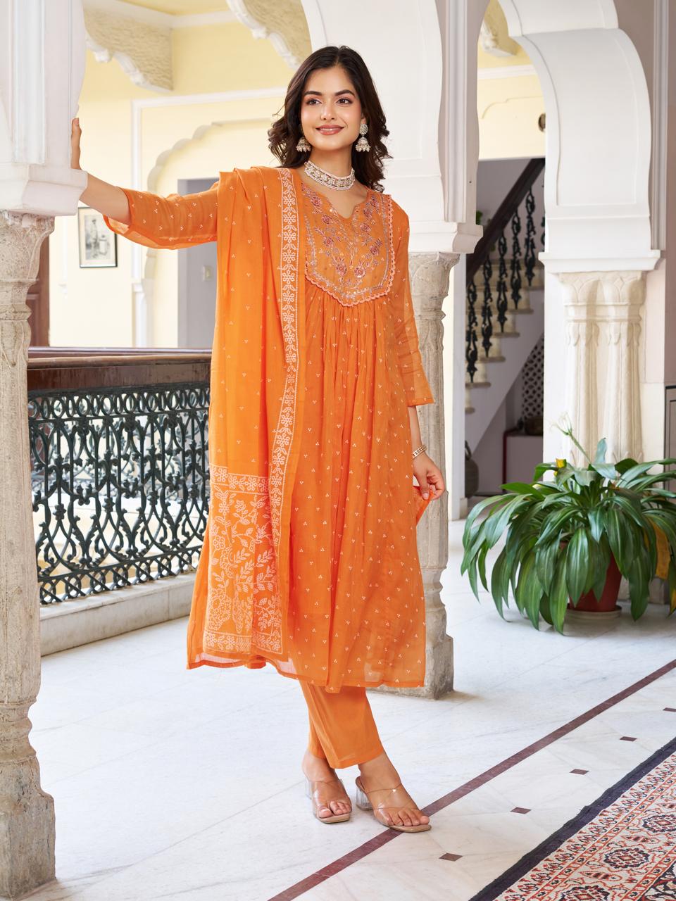 Full shot of a model standing confidently in an orange embroidered cotton kurti set in a traditional Indian architectural setting.