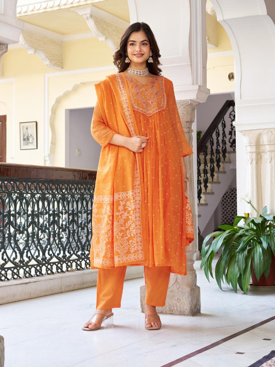 Model in an orange kurti set, hands clasped, posing gracefully, offering a complete view of the elegant three-piece ensemble.
