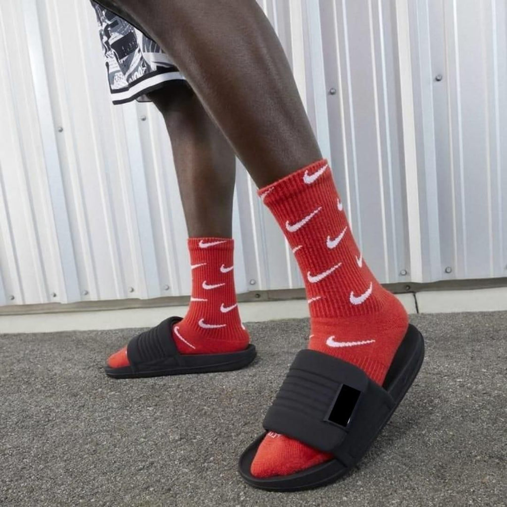 Person wearing red socks with white Nike logos and black slides on a gray pavement.