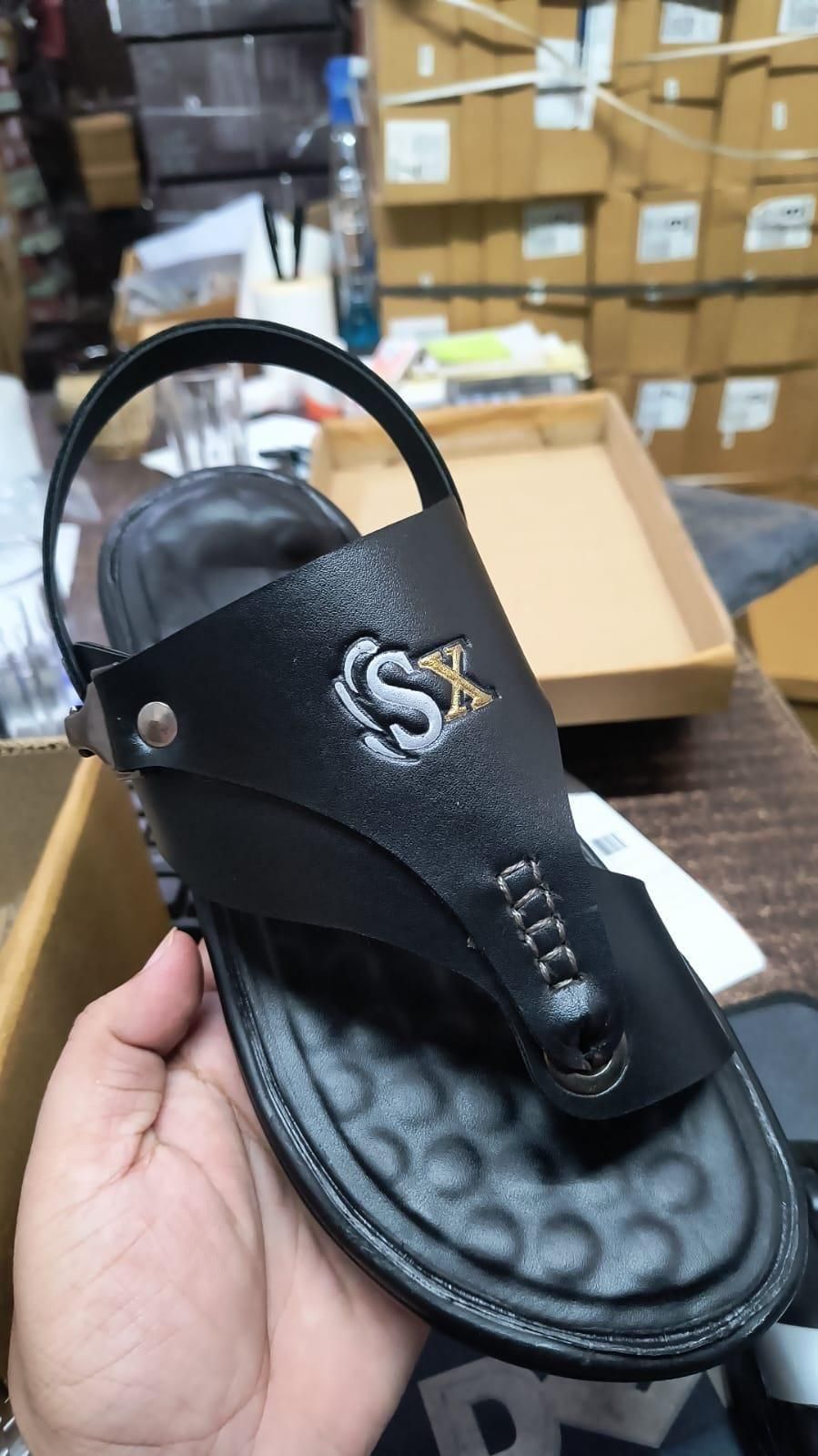 Black sandal with 'SX' logo held by a hand in a warehouse setting