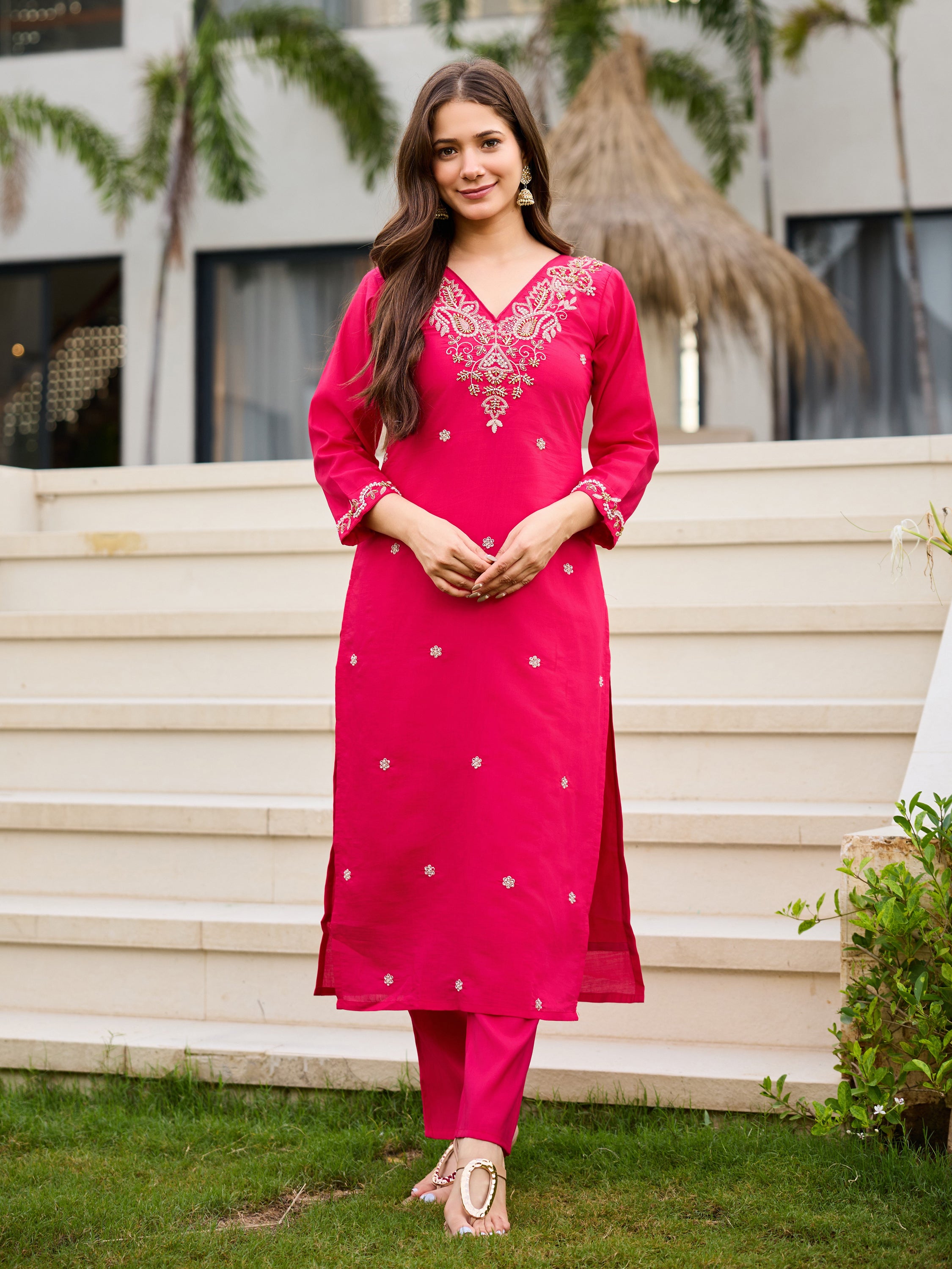 Full body shot of a woman smiling, standing front, wearing the pink Roman silk embroidered kurti set, outdoors.