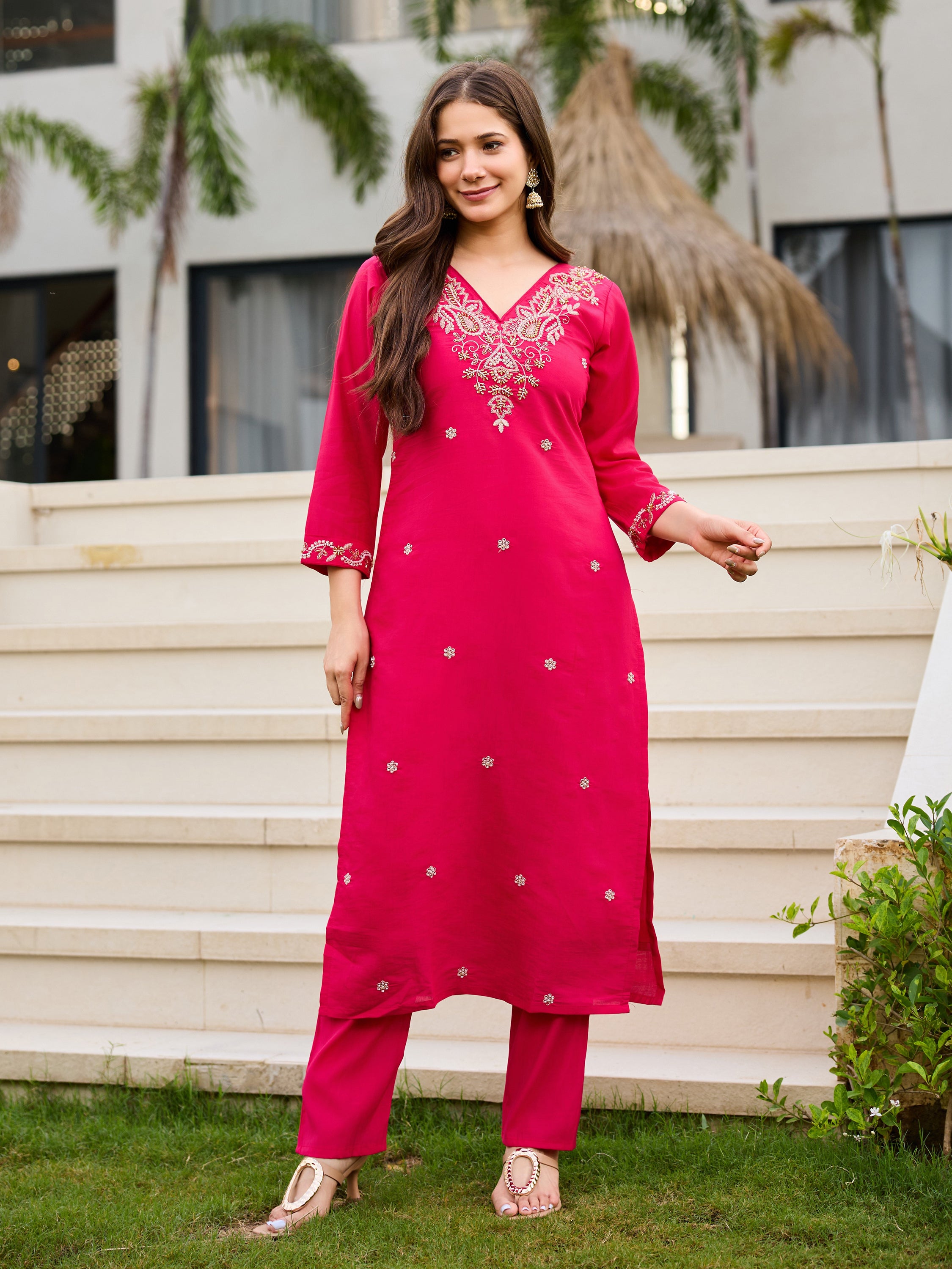 Woman in pink Roman silk kurti set, standing slightly angled, showcasing the full ensemble in an outdoor garden.