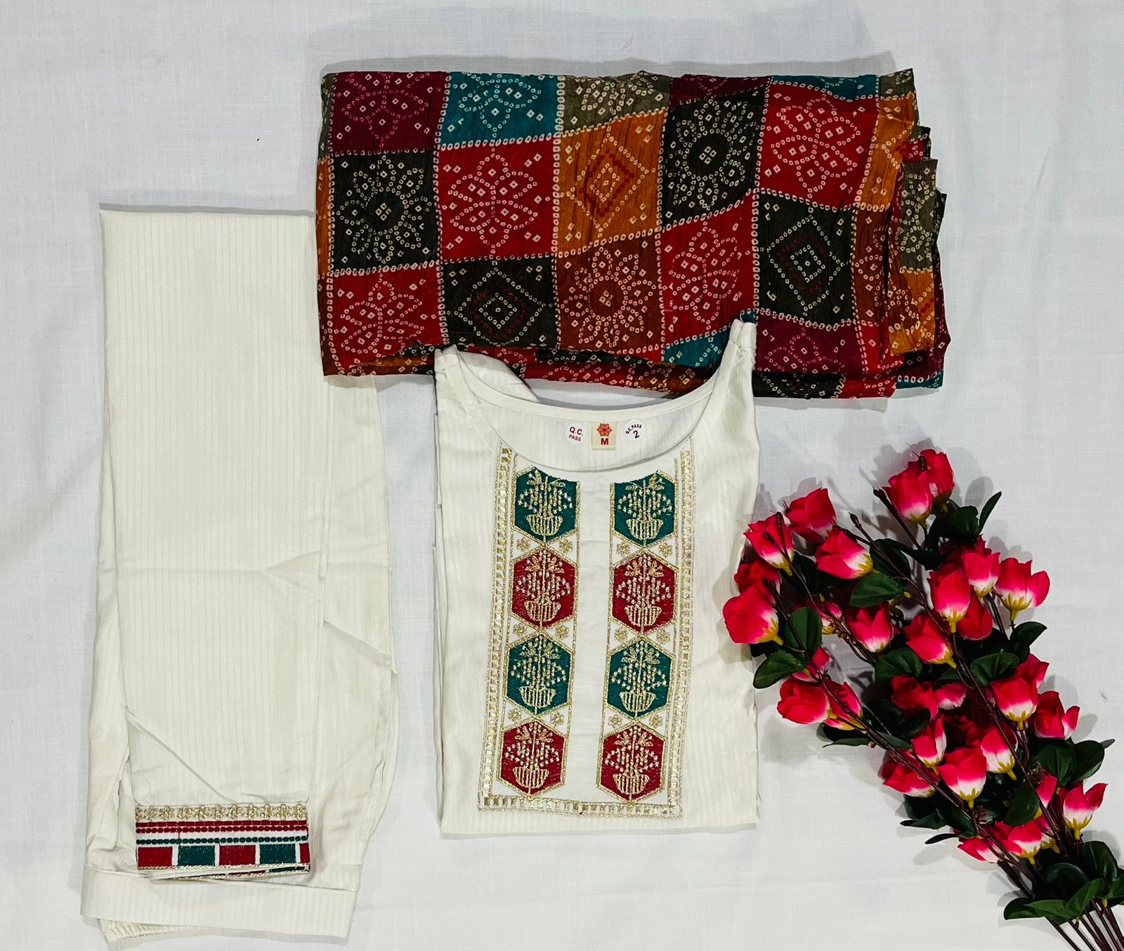 Overhead view of TRENDBUY D488 Off-White Kurta Set, folded kurta and pants with colorful dupatta, accented with red flowers.