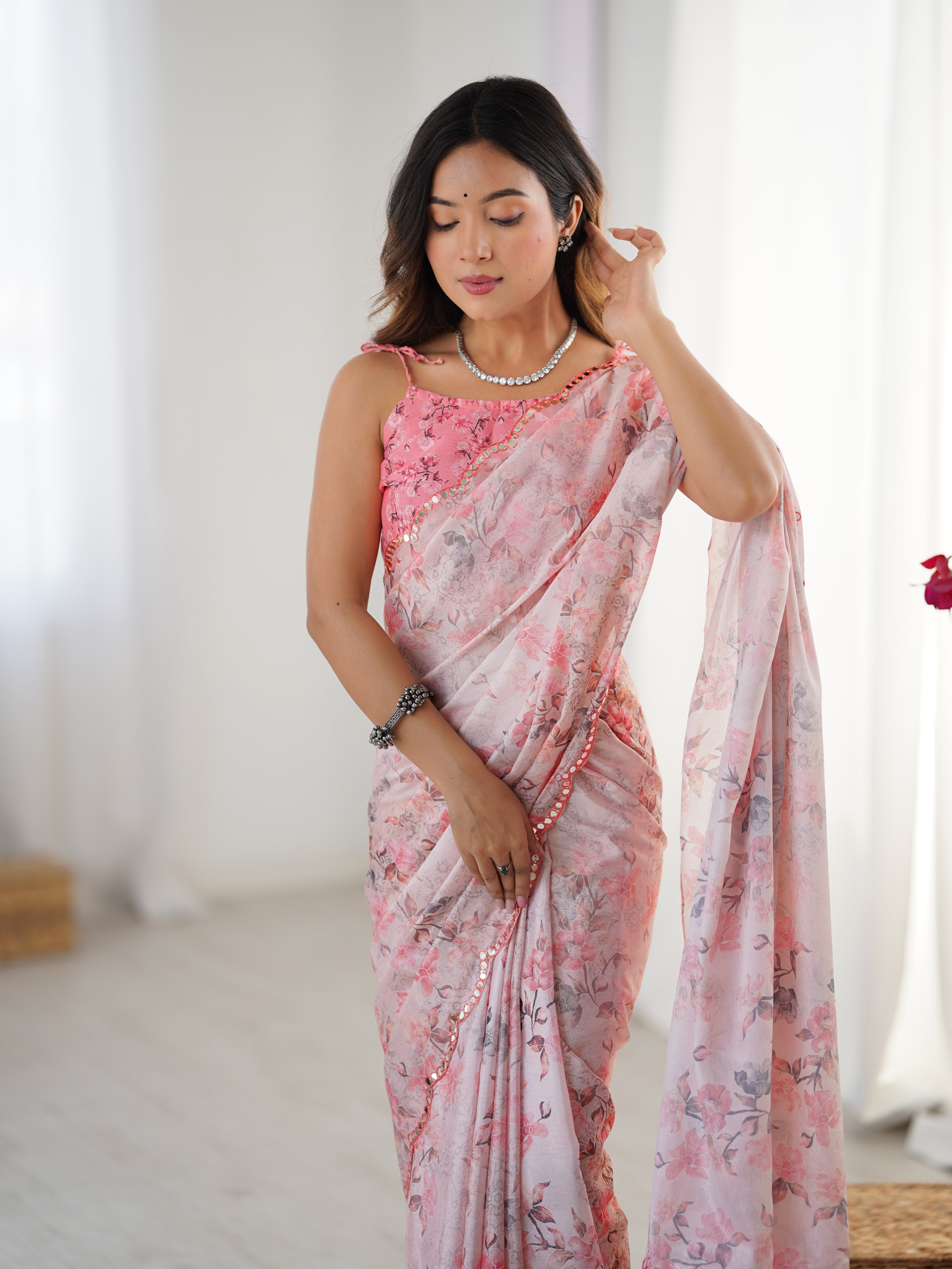 Close-up of model adjusting her hair, highlighting the pink floral saree's print and mirror-embellished border.