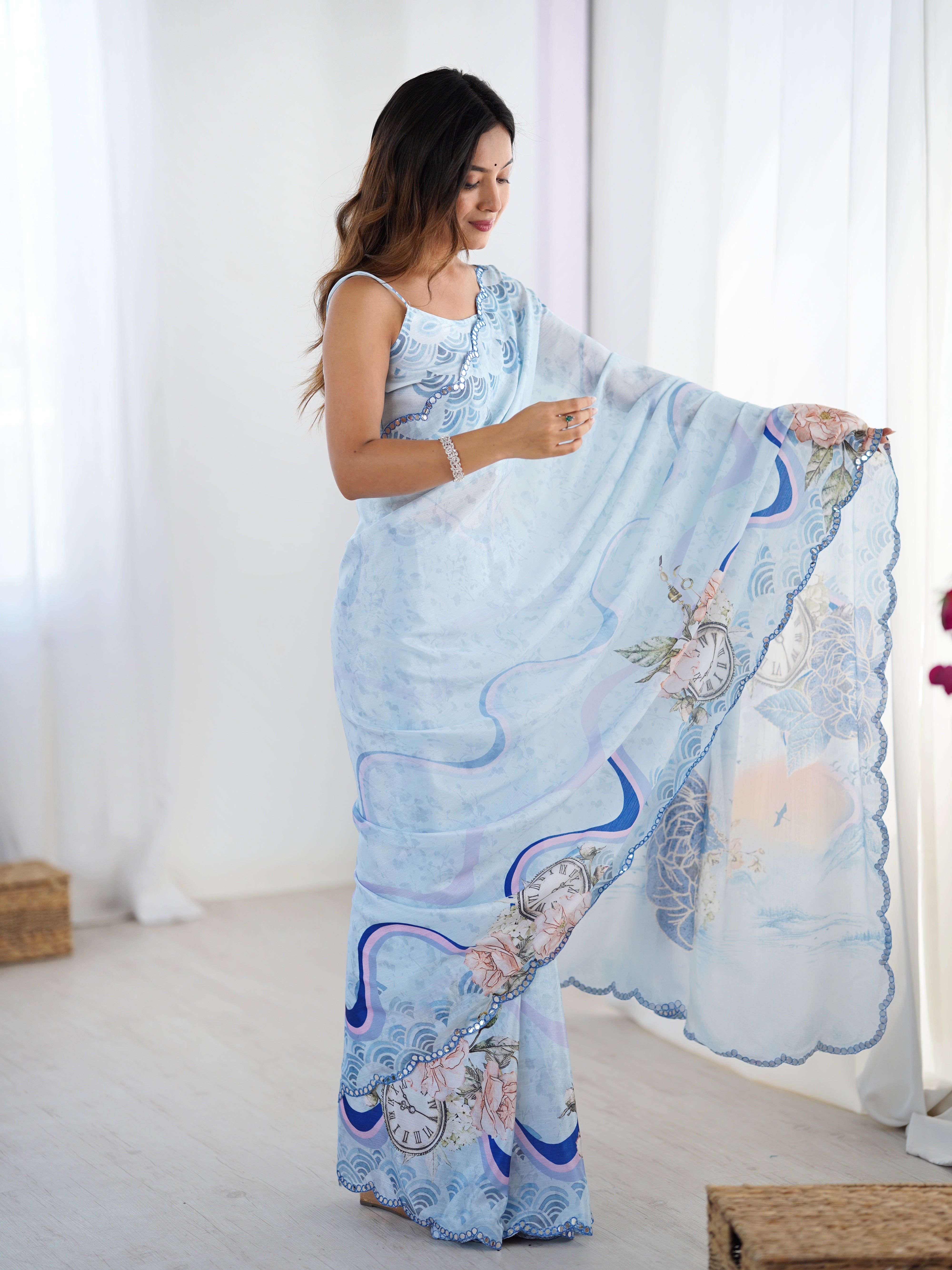 Full length shot of a woman in a pastel blue Chinnon saree with floral and clock prints, emphasizing the unique mirror-embellished border details.