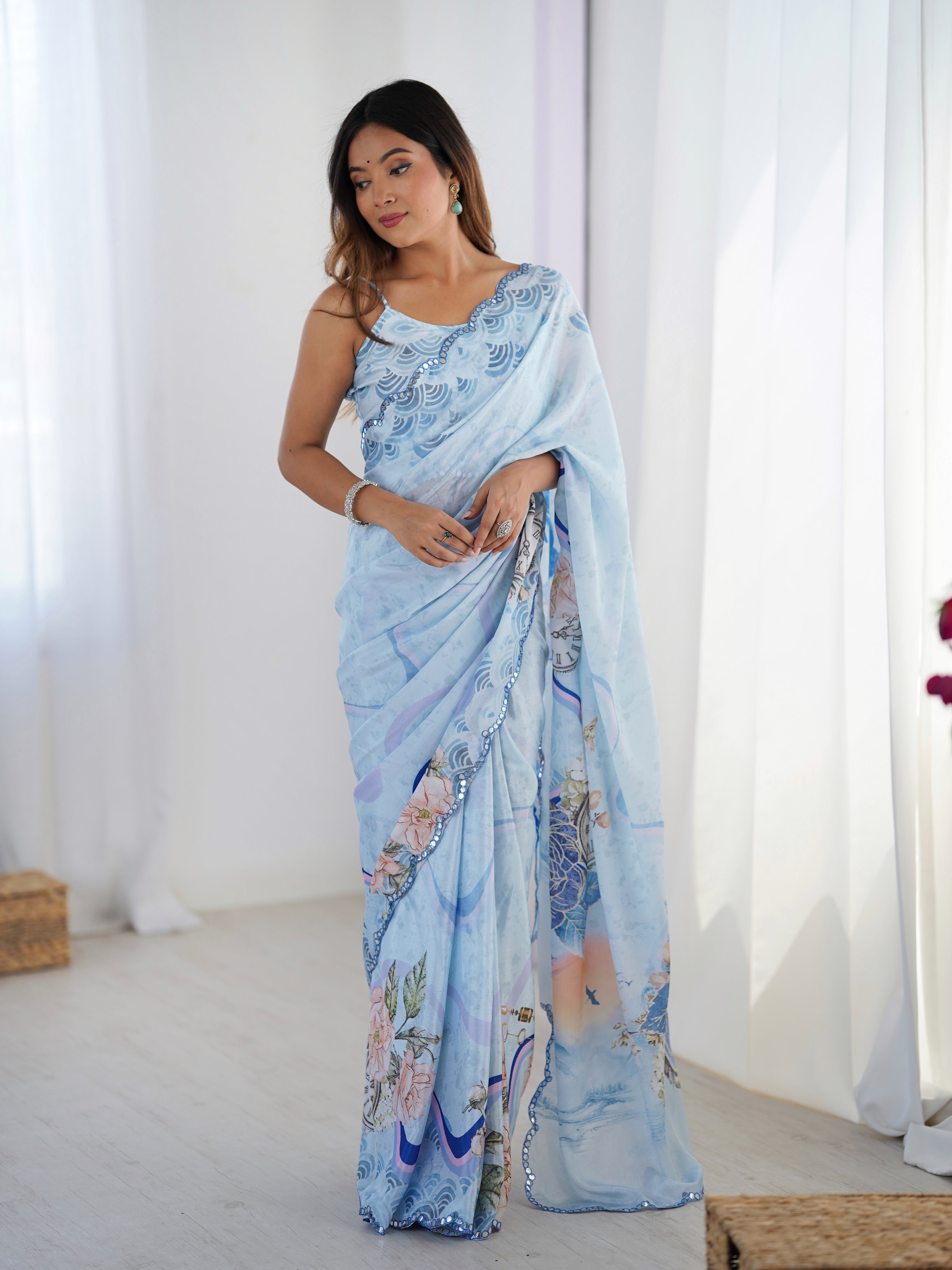 Woman looking down, elegantly presenting the full silhouette of the sky blue Chinnon saree with decorative mirror work, perfect for festive occasions.