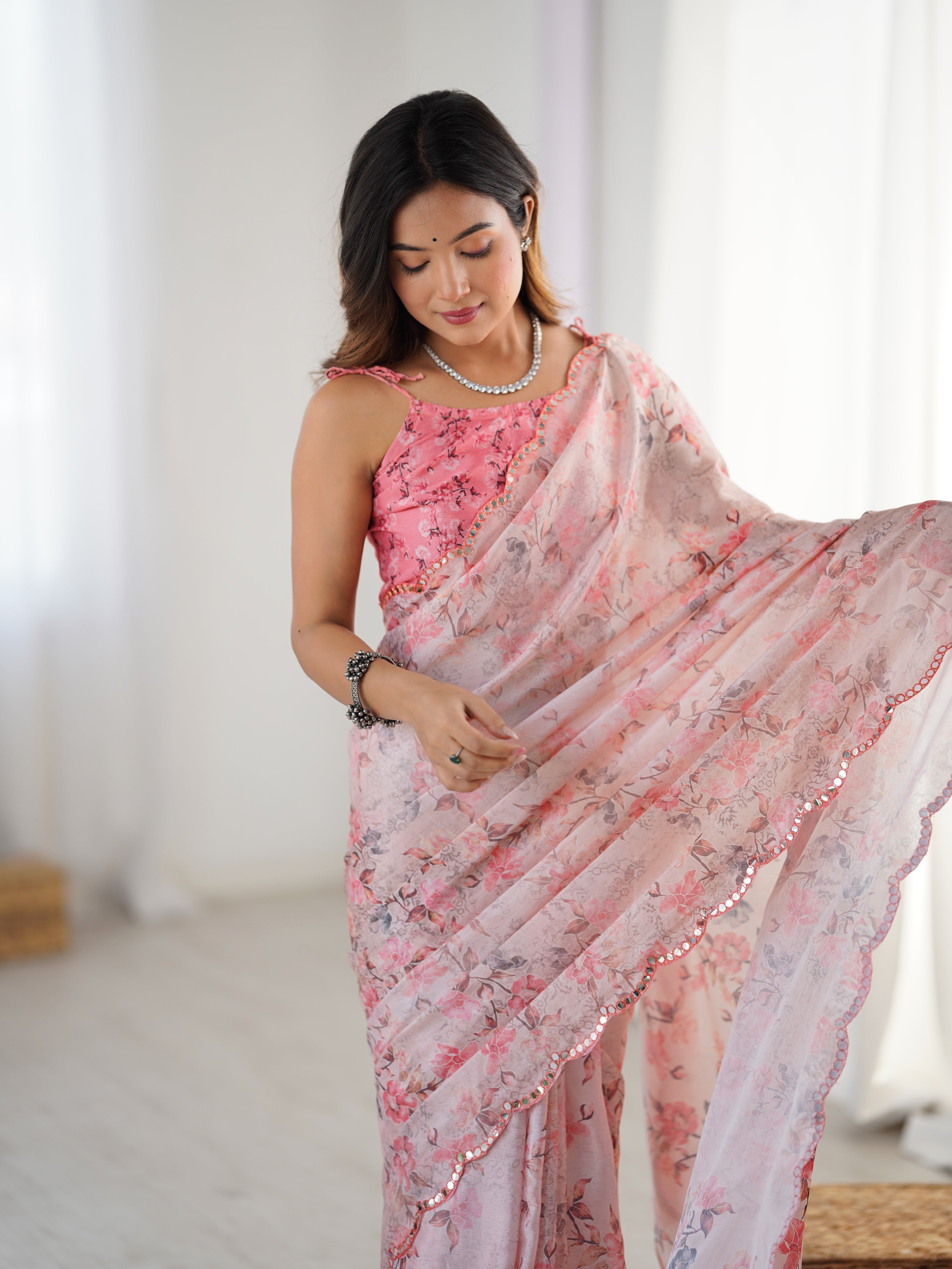 Close-up of the model admiring the delicate floral print and the intricate kutchi mirror work lace border of the TRENDBUY chinnon saree.