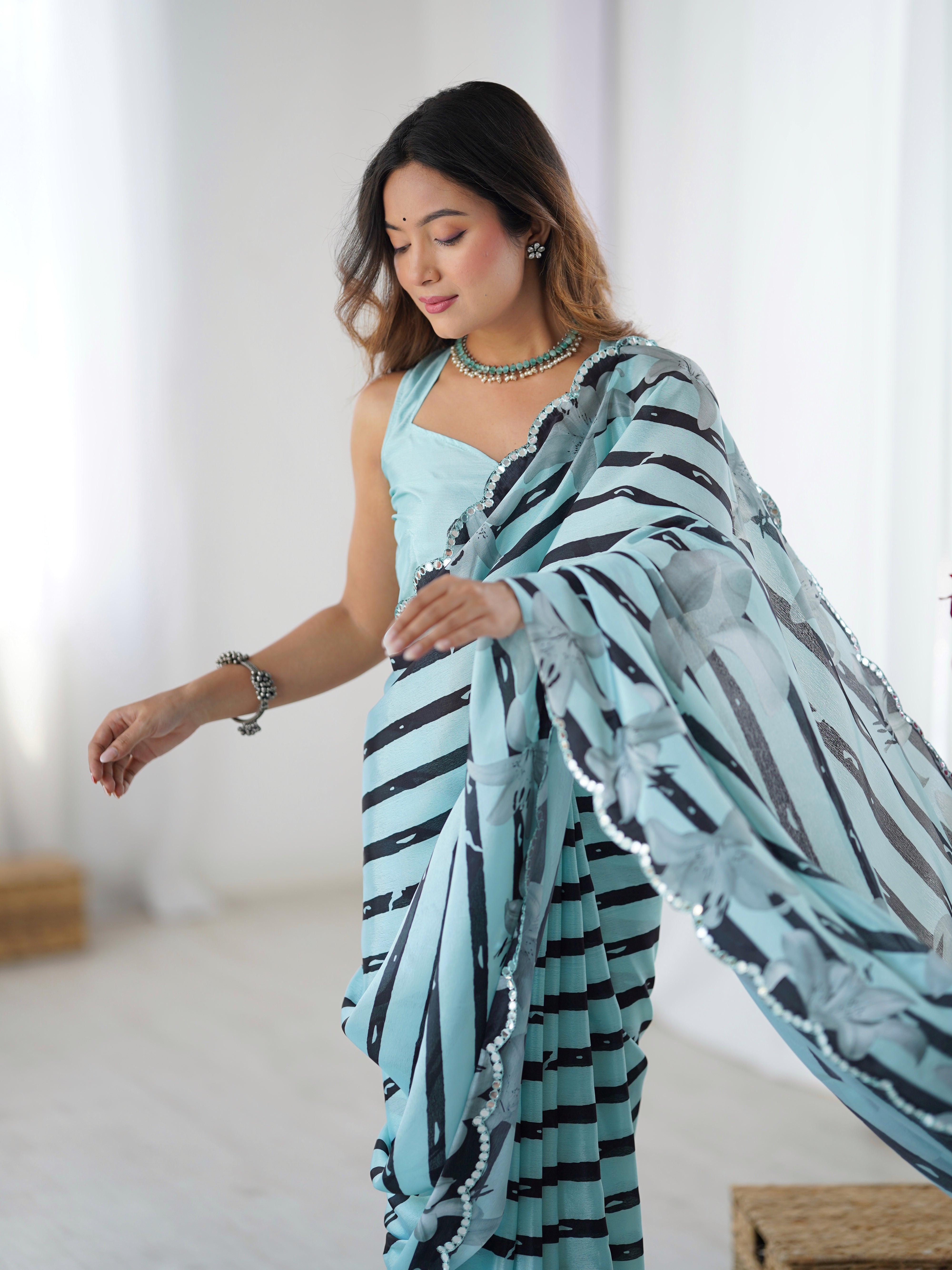 Side view of a woman showcasing the intricate Kutchi mirror lace border on a beautiful aqua blue Chinnon saree from TRENDBUY.