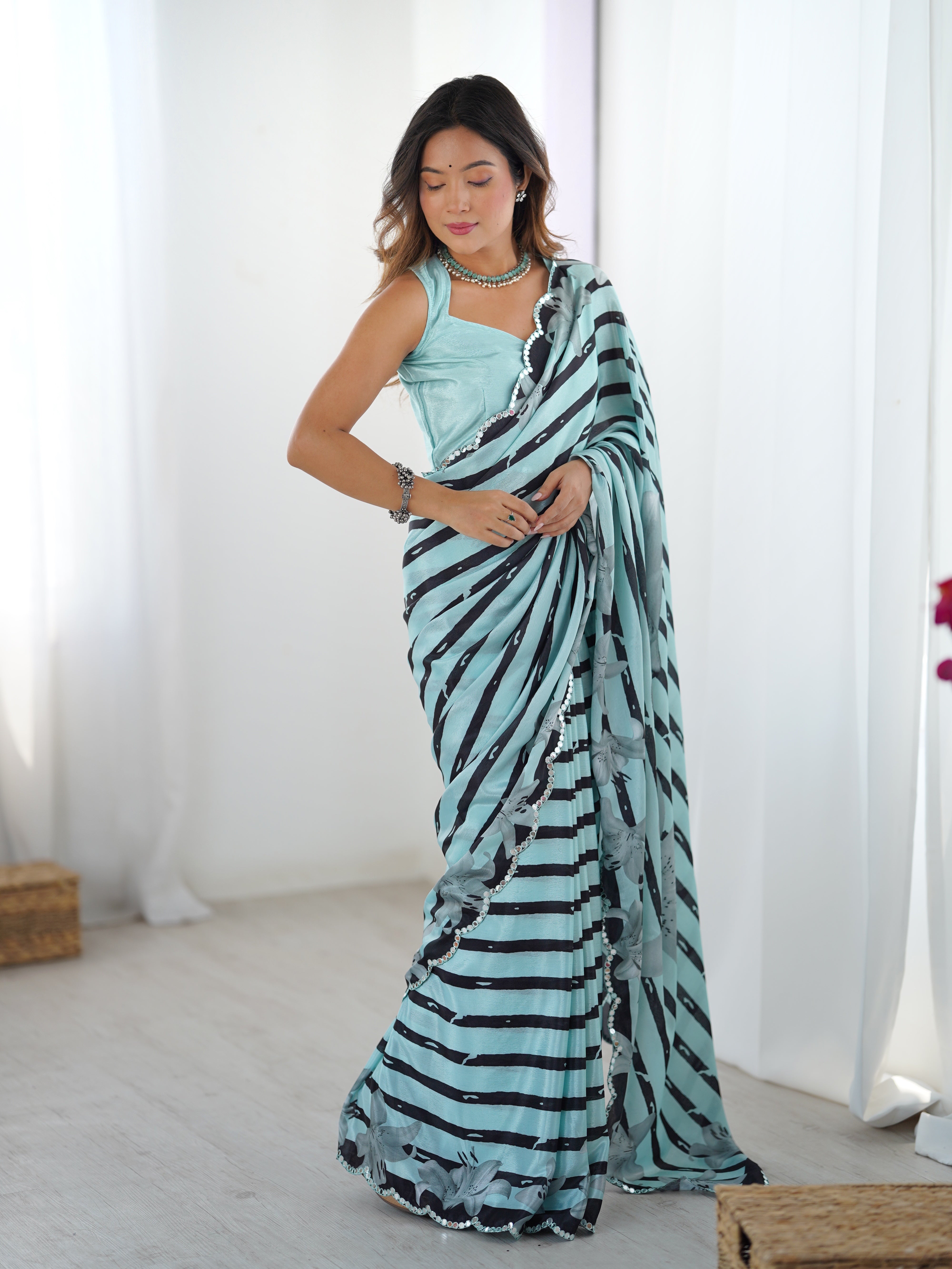 TRENDBUY model looking down, displaying the full length and fluid movement of the aqua blue striped Chinnon saree with mirror embellishments.