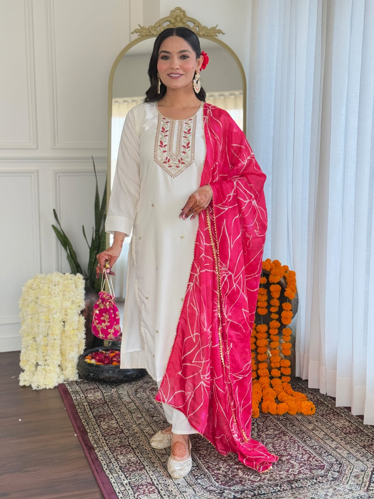 Full length front view of a TRENDBUY model gracefully posing in a white embroidered kurti set and a vibrant pink dupatta, against a decorative background.