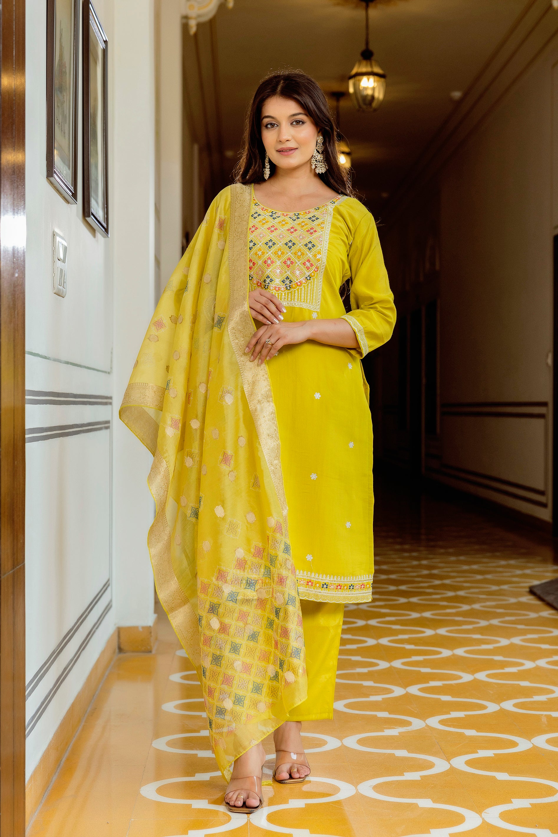 Model showcasing the full yellow embroidered Viscose Shimar kurta set with multi-color work and a shimmering dupatta, standing elegantly in a traditional setting.