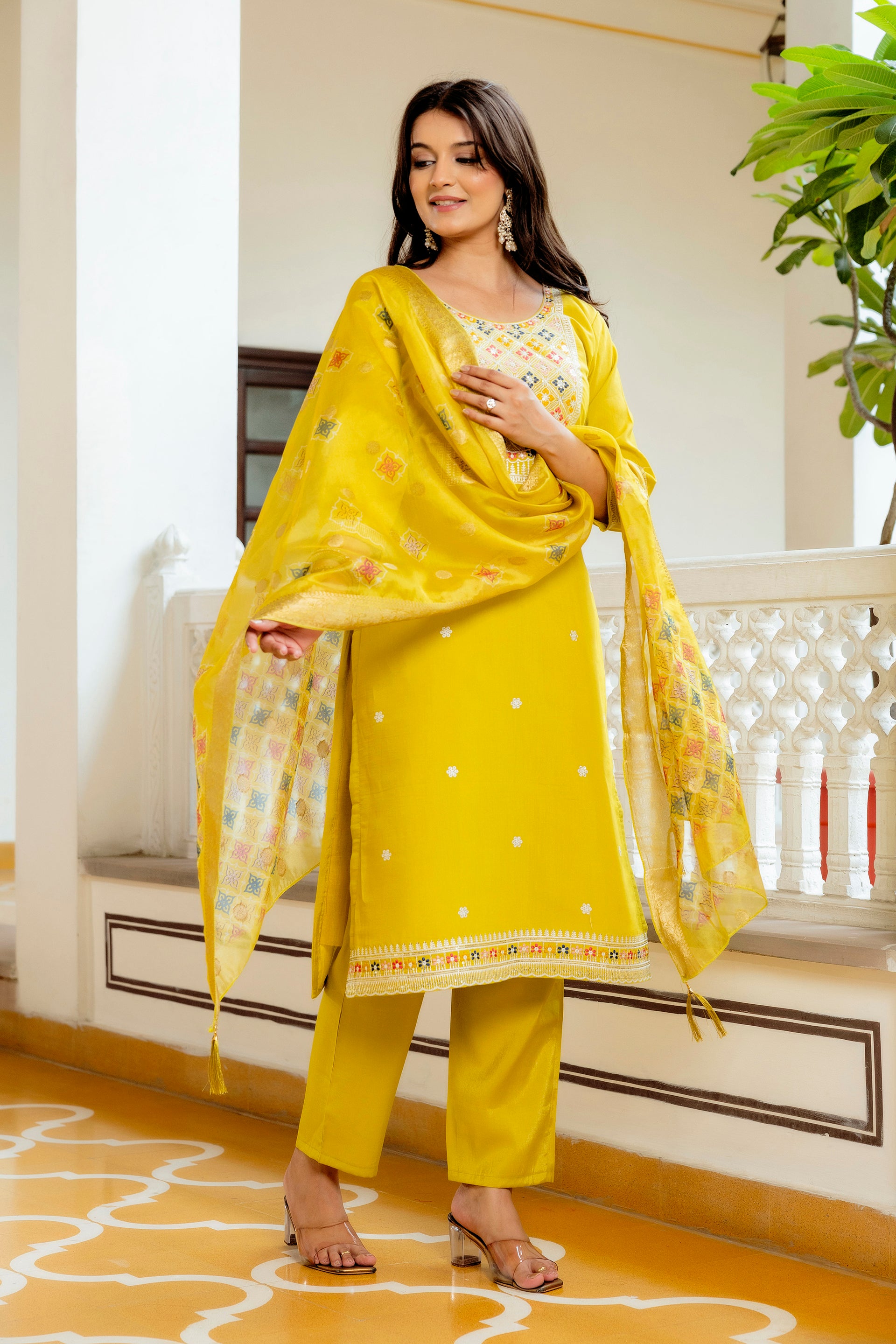 Model gently adjusting the draped yellow embroidered dupatta of the kurta set, capturing its vibrant multi-color jacquard pattern and gold border detail.