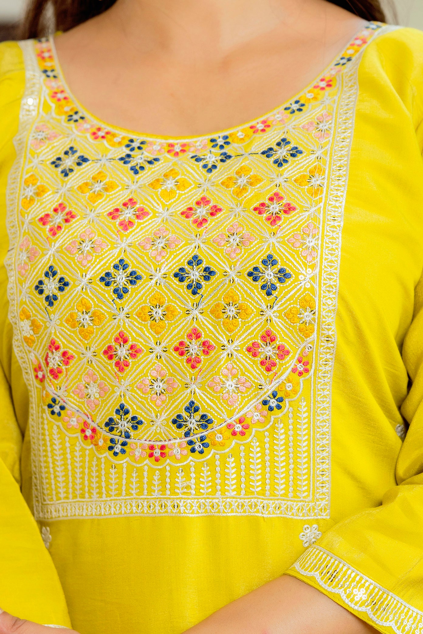 Extreme close-up of the exquisite multi-color geometric and floral embroidery on the neckline and yoke of the yellow Viscose Shimar kurti.