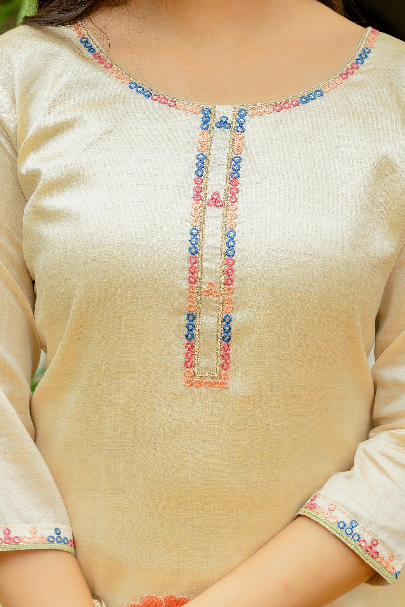 Detailed view of the embellished placket and round neckline of the beige kurta, featuring delicate embroidered beadwork in colorful patterns.