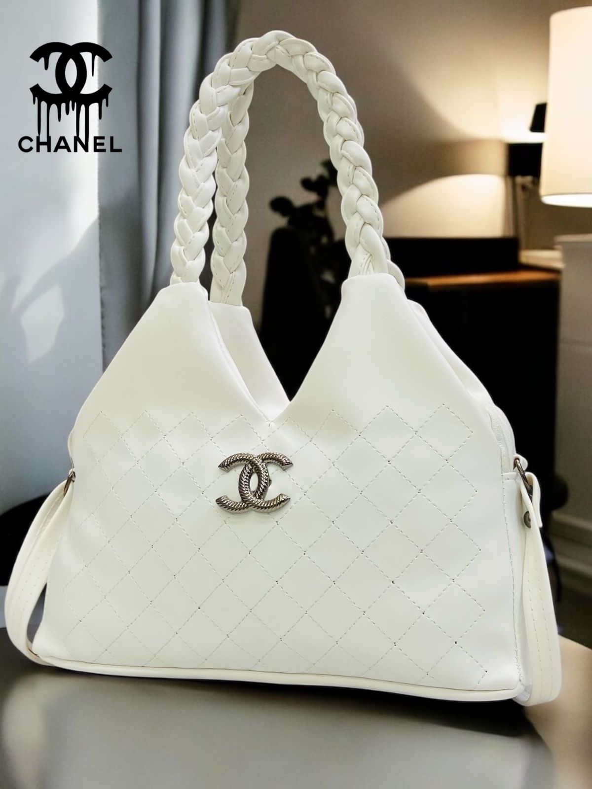 White quilted handbag with braided handles and Chanel logo on a blurred indoor background