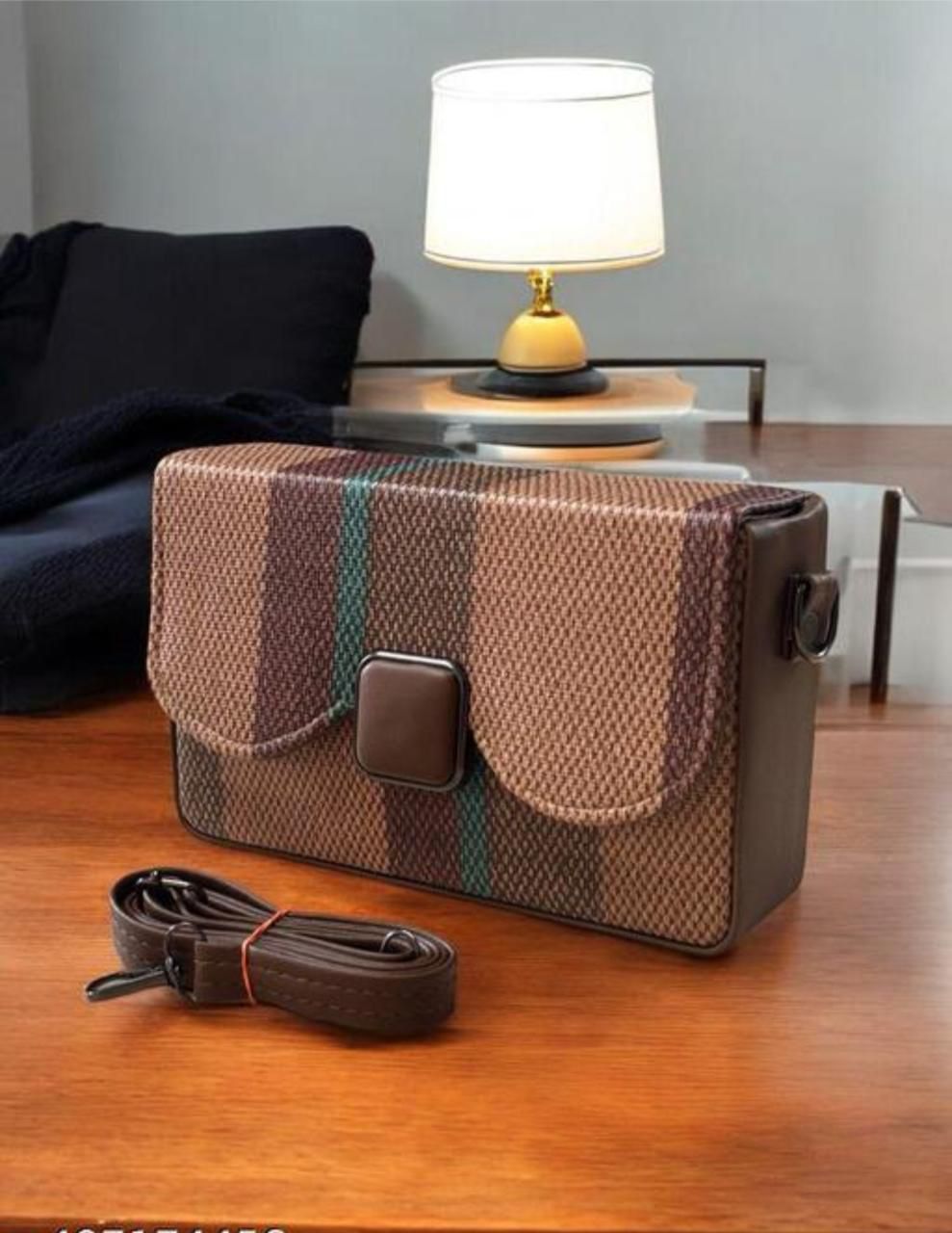 Brown textured handbag with plaid strap on a wooden surface, lamp in the background