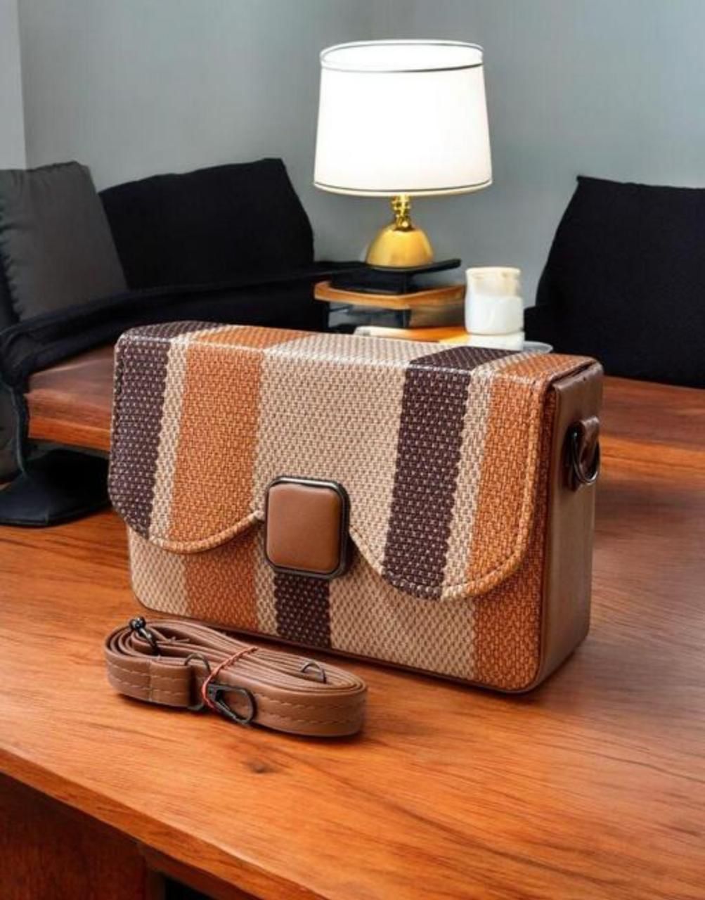 Patterned handbag on a wooden surface with a lamp and candle in the background