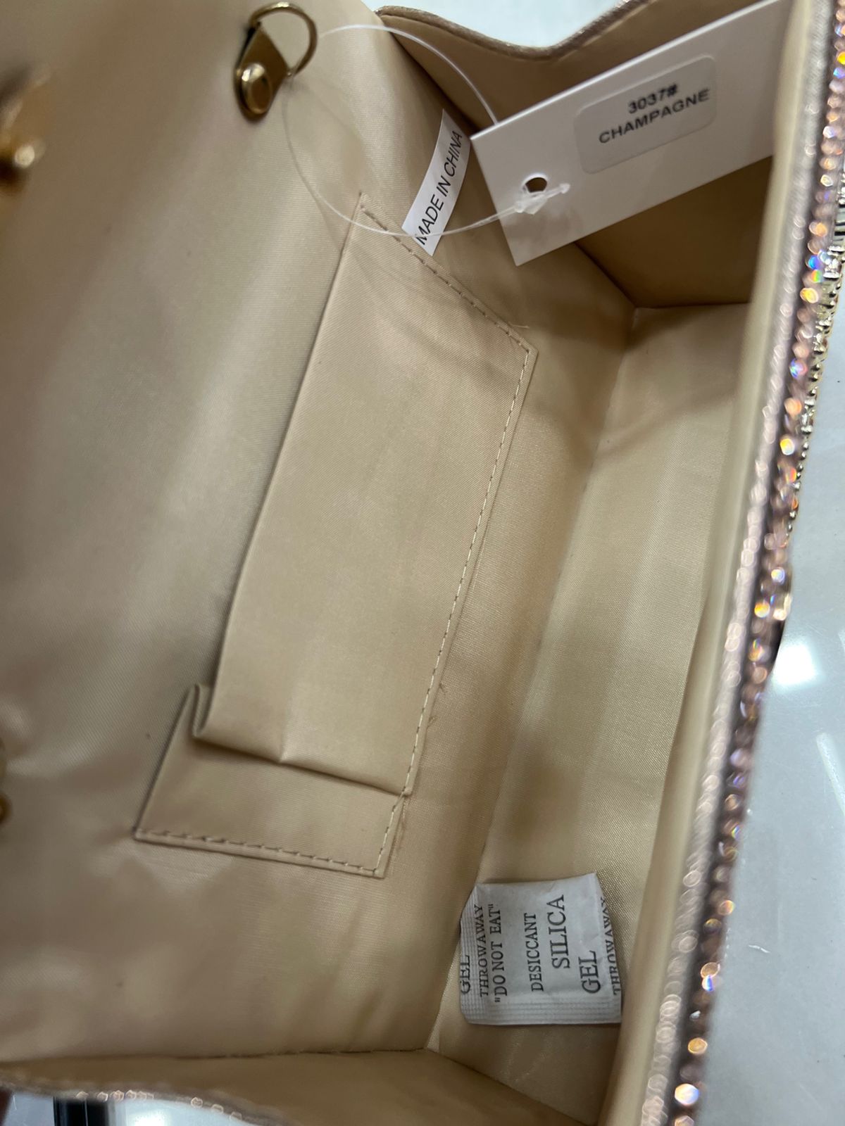 Close-up of a beige handbag with visible labels and rhinestone detailing.