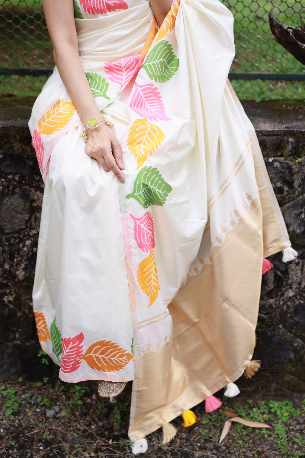 Close-up of intricate multicolor leaf zari woven patterns on soft white fabric.