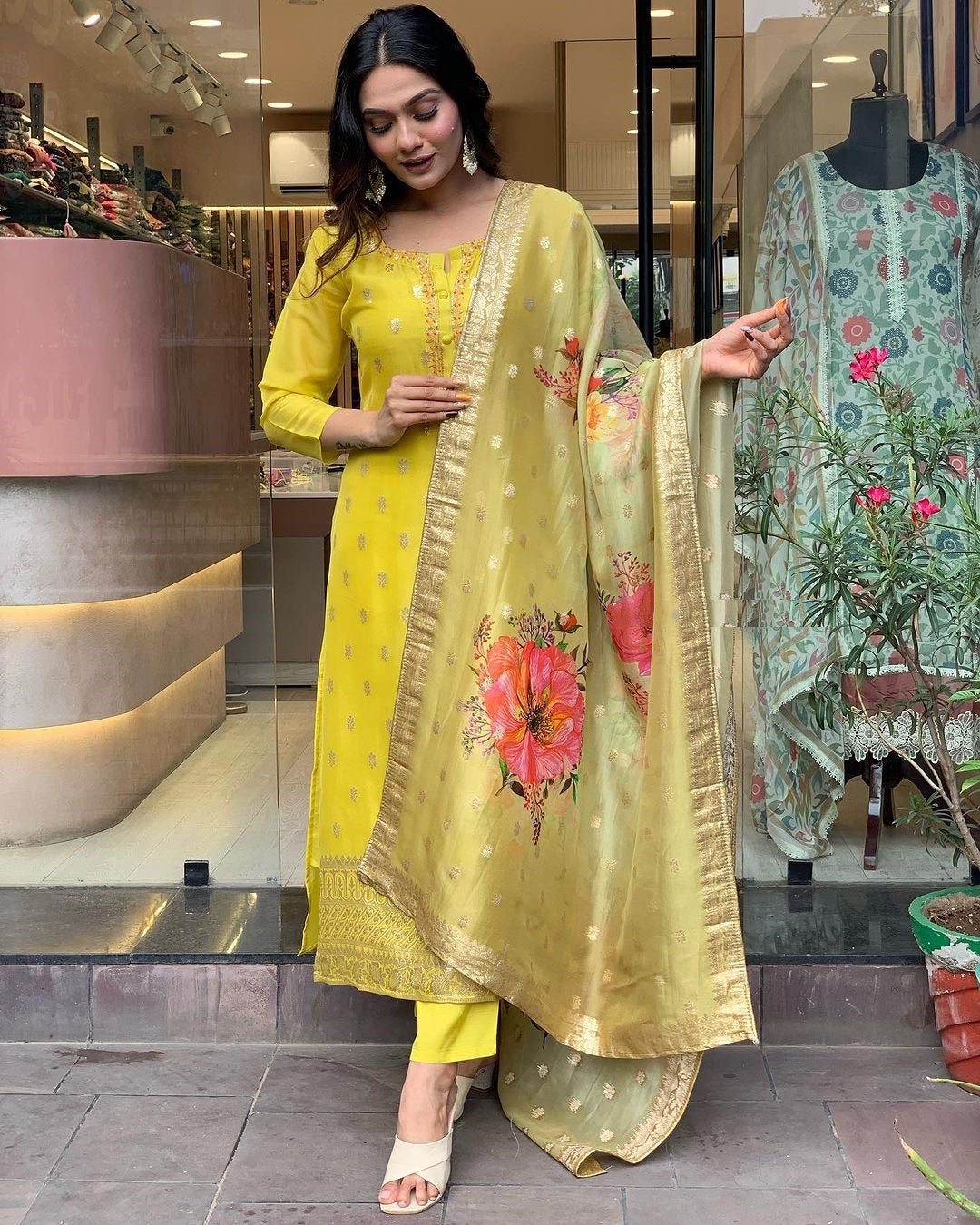 Woman in yellow embroidered kurti set with floral dupatta, standing outdoors.