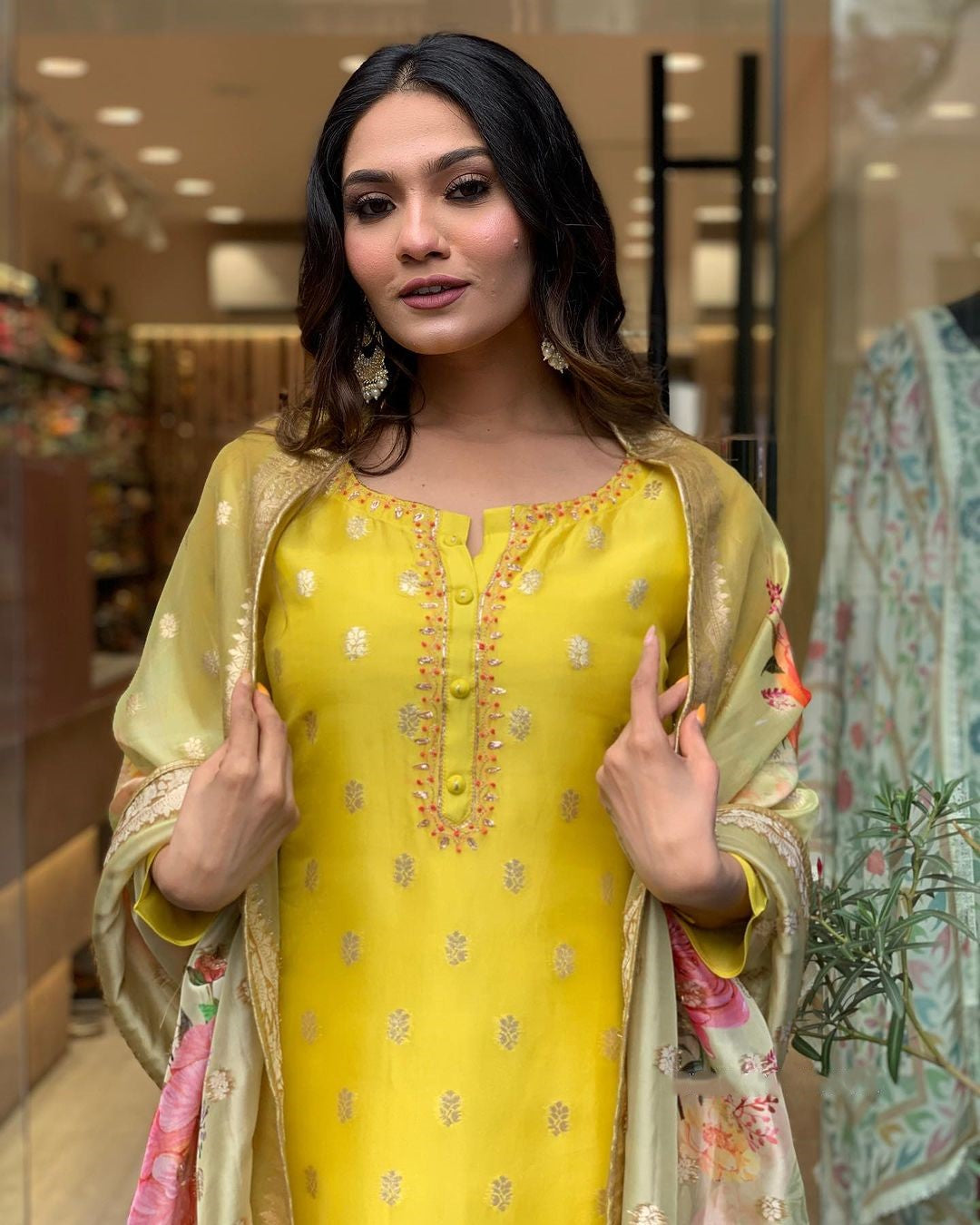 Direct gaze from the woman, displaying the complete yellow embroidered kurti and floral dupatta ensemble with confidence.
