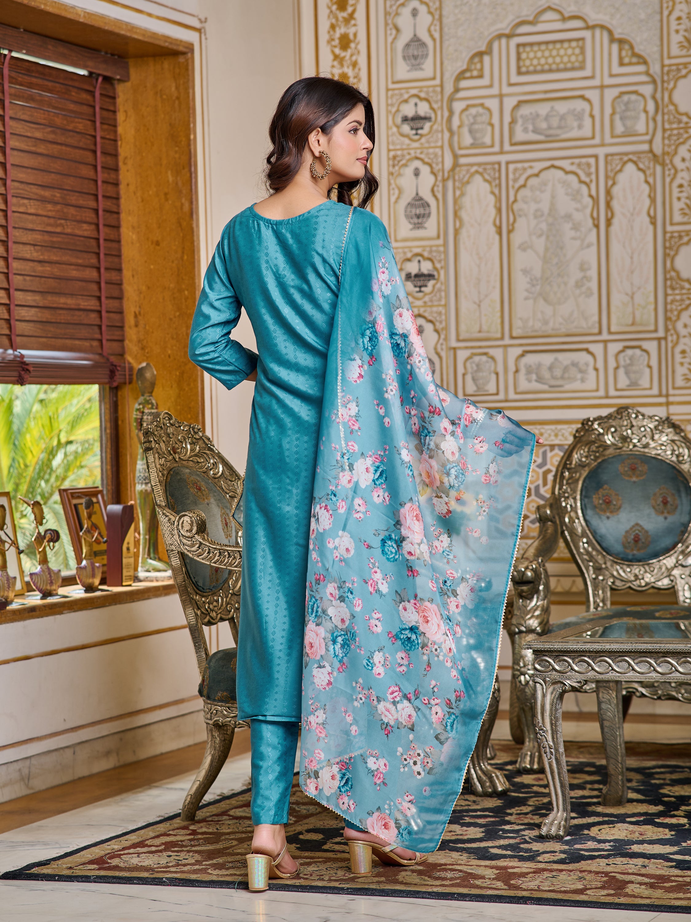 Rear view of the model presenting the back of the teal embroidered kurta and the flowing digital print dupatta.
