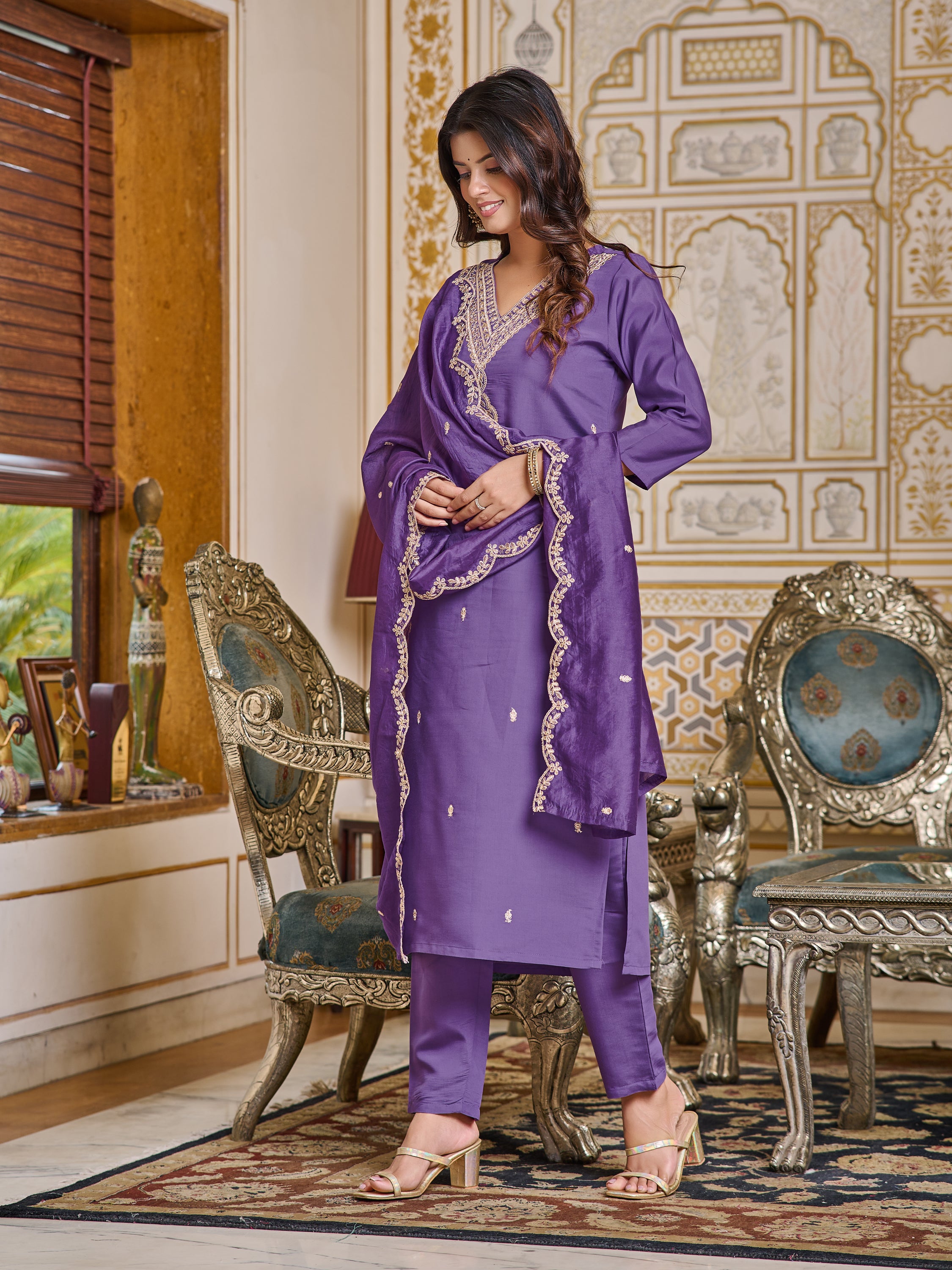Woman with hands crossed, looking down, showing side profile and full kurti set with dupatta.