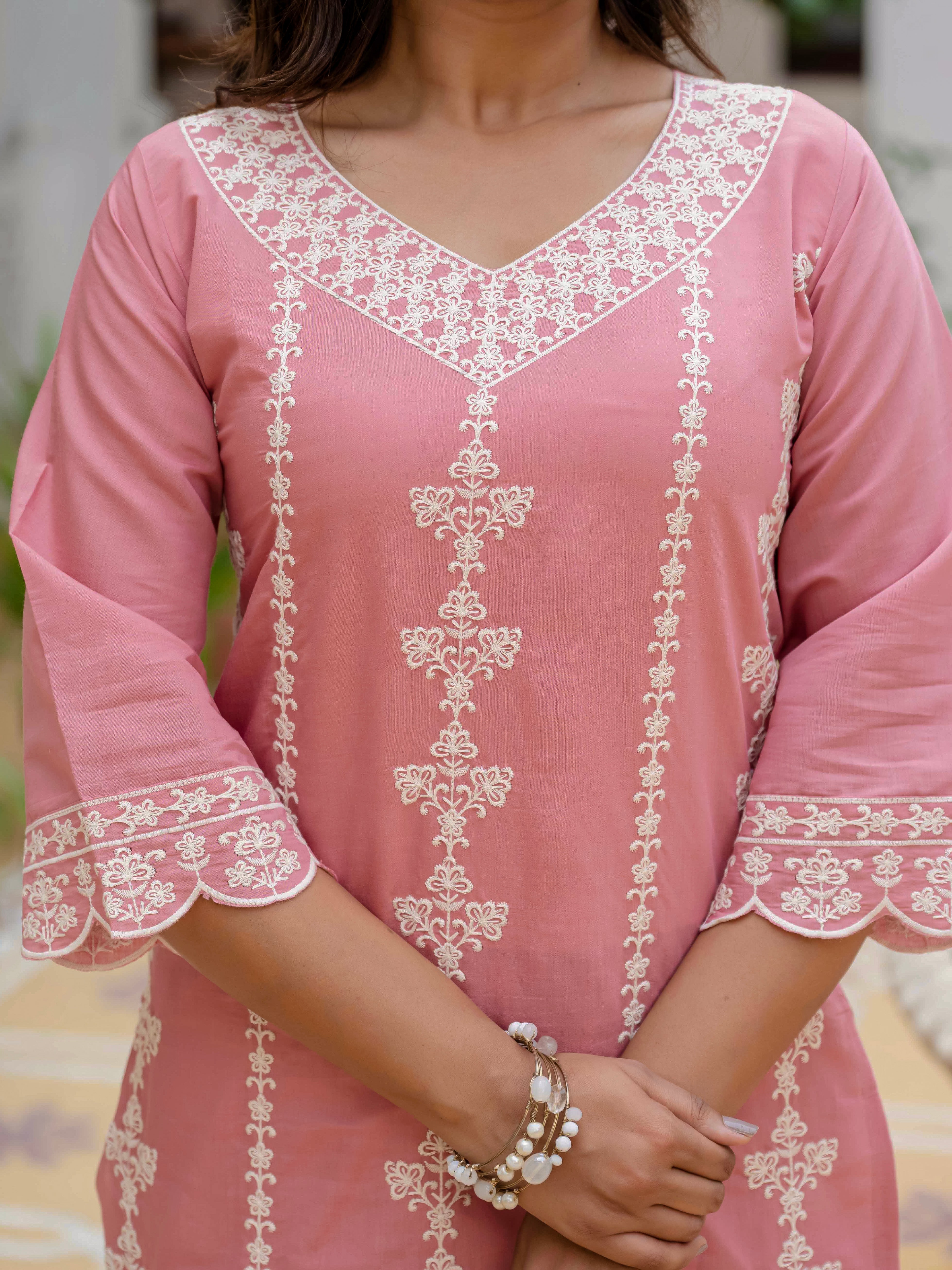 Close-up of a woman wearing a rose pink Roman silk kurti with intricate white embroidery on the V-neck and front panel, showcasing design details.