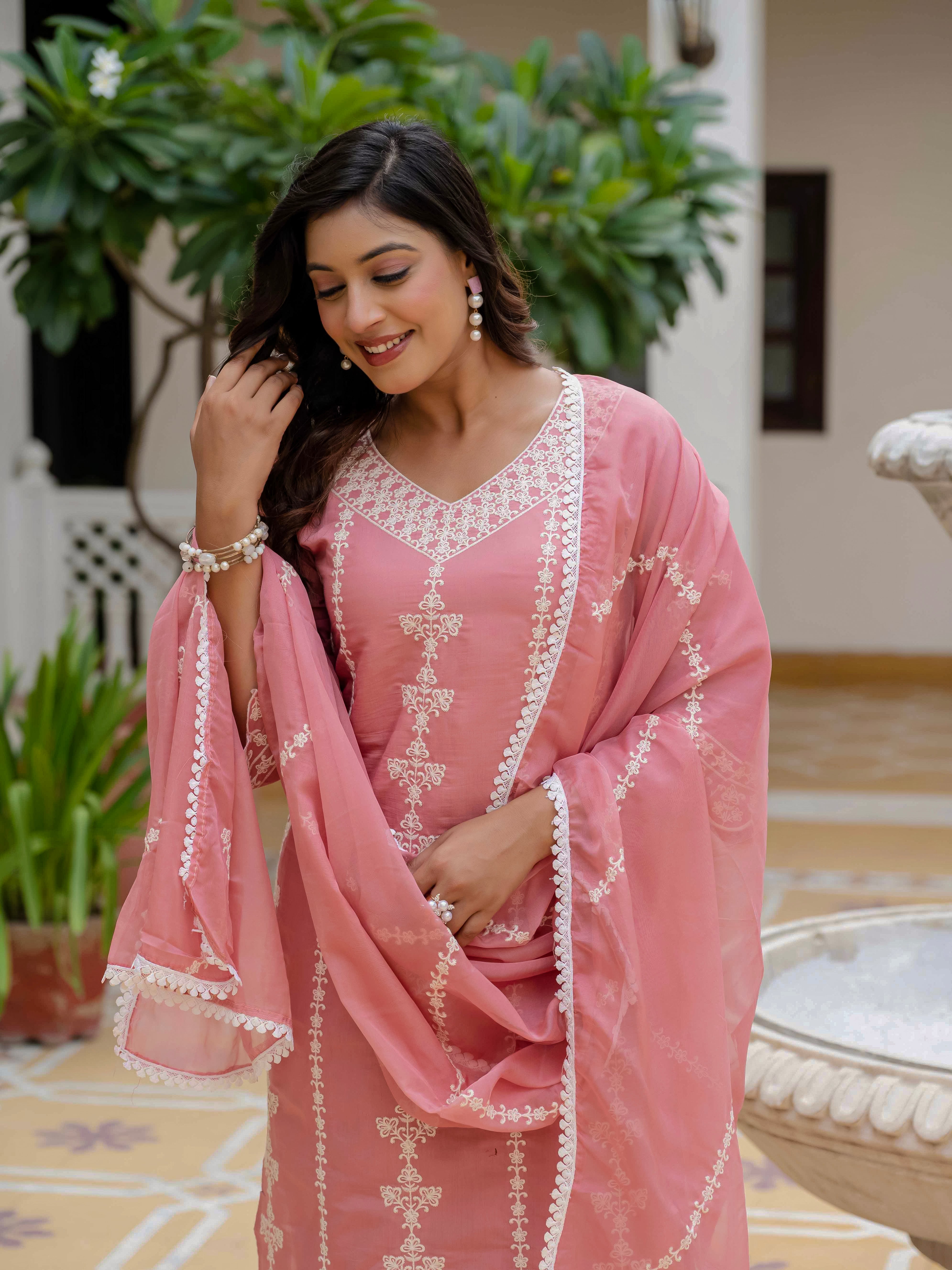 Close-up portrait of a smiling woman in a rose pink embroidered kurti set, highlighting the detailed neckline, delicate jewelry, and overall cheerful expression.