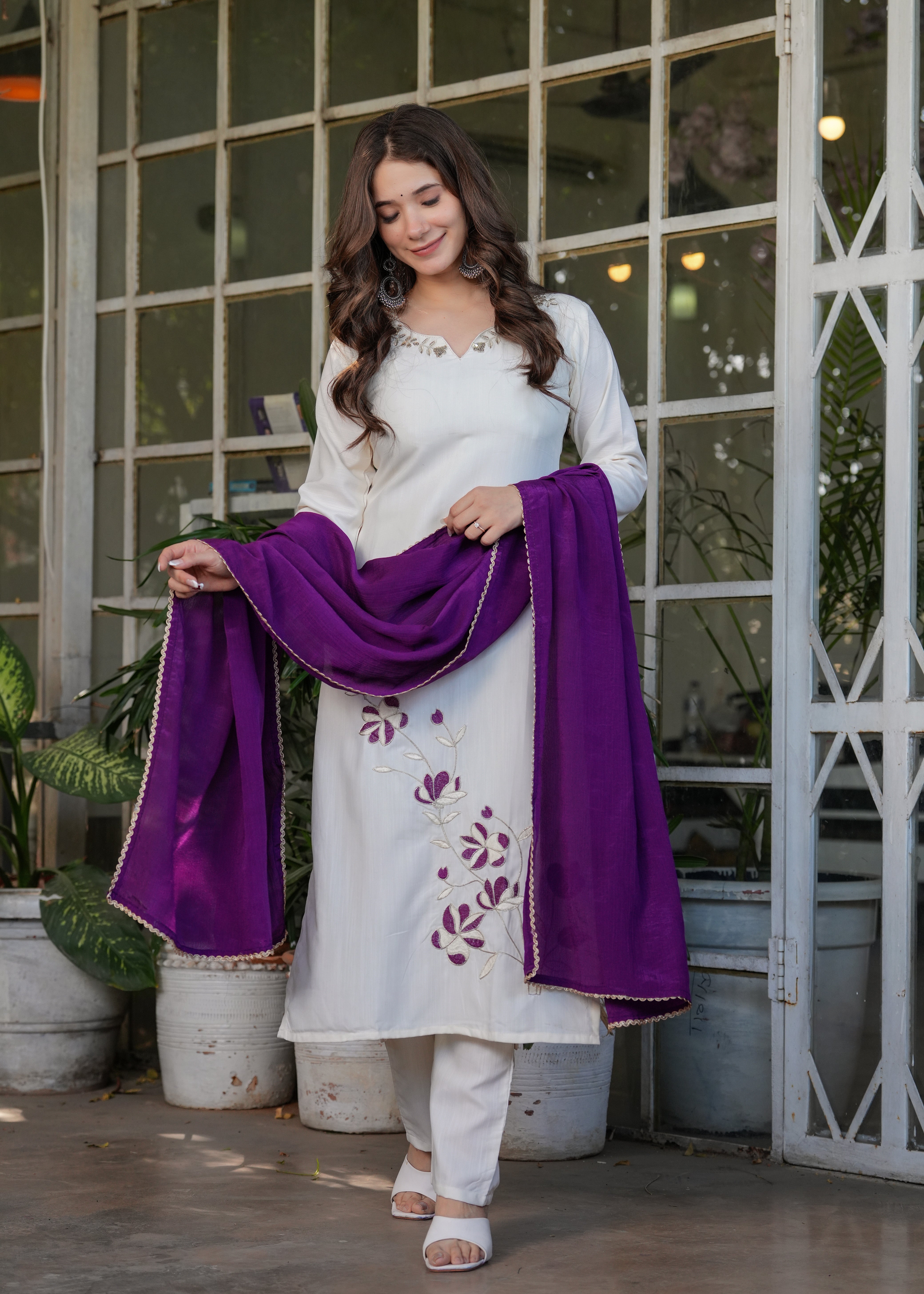 Woman holding a purple chinon dupatta over an off-white embroidered kurta and pant set, showing the outfit's flow and color contrast.