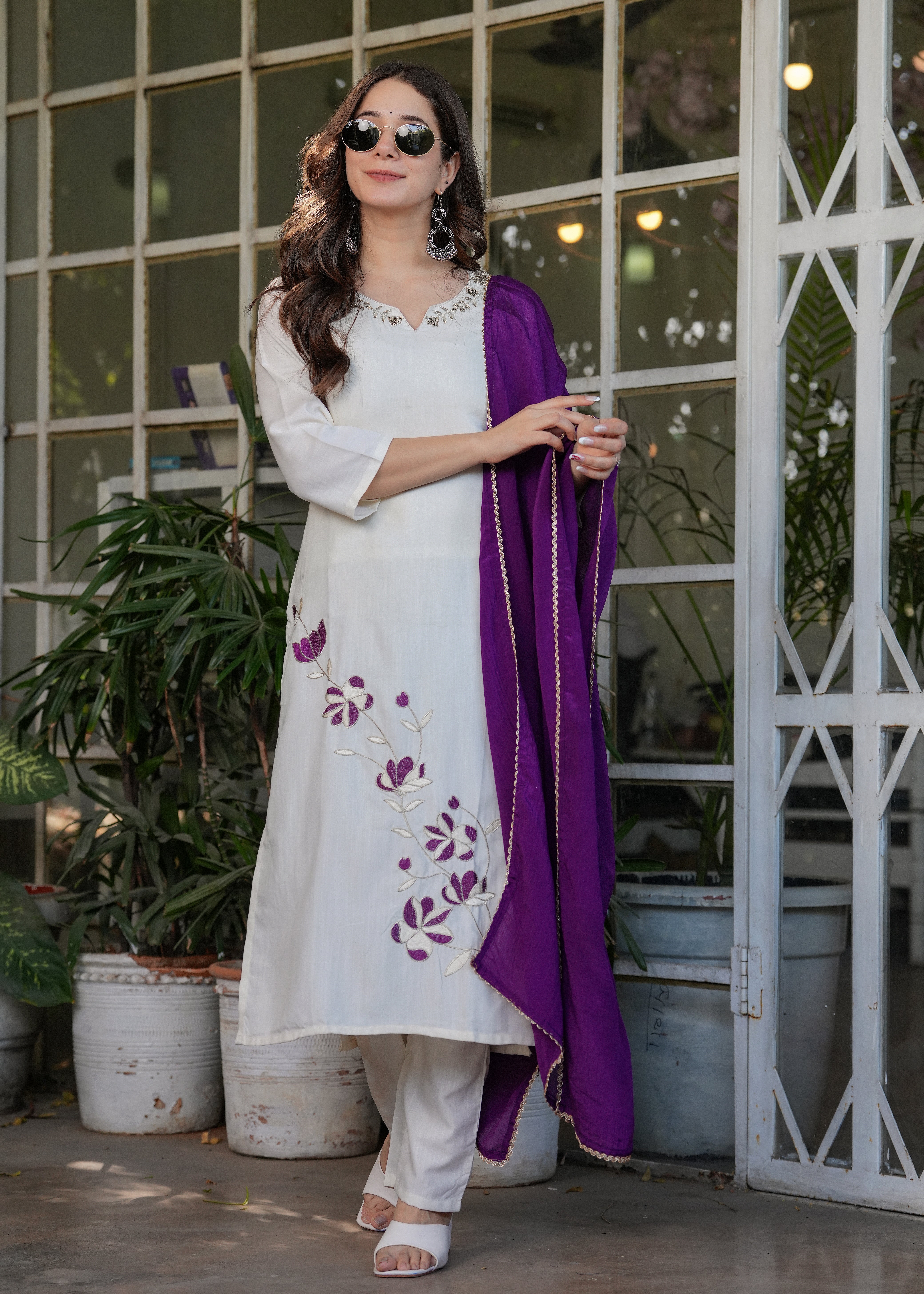 Woman confidently posing in a chic off-white kurta set, contrasting purple dupatta adding a pop of color, a TRENDBUY statement.