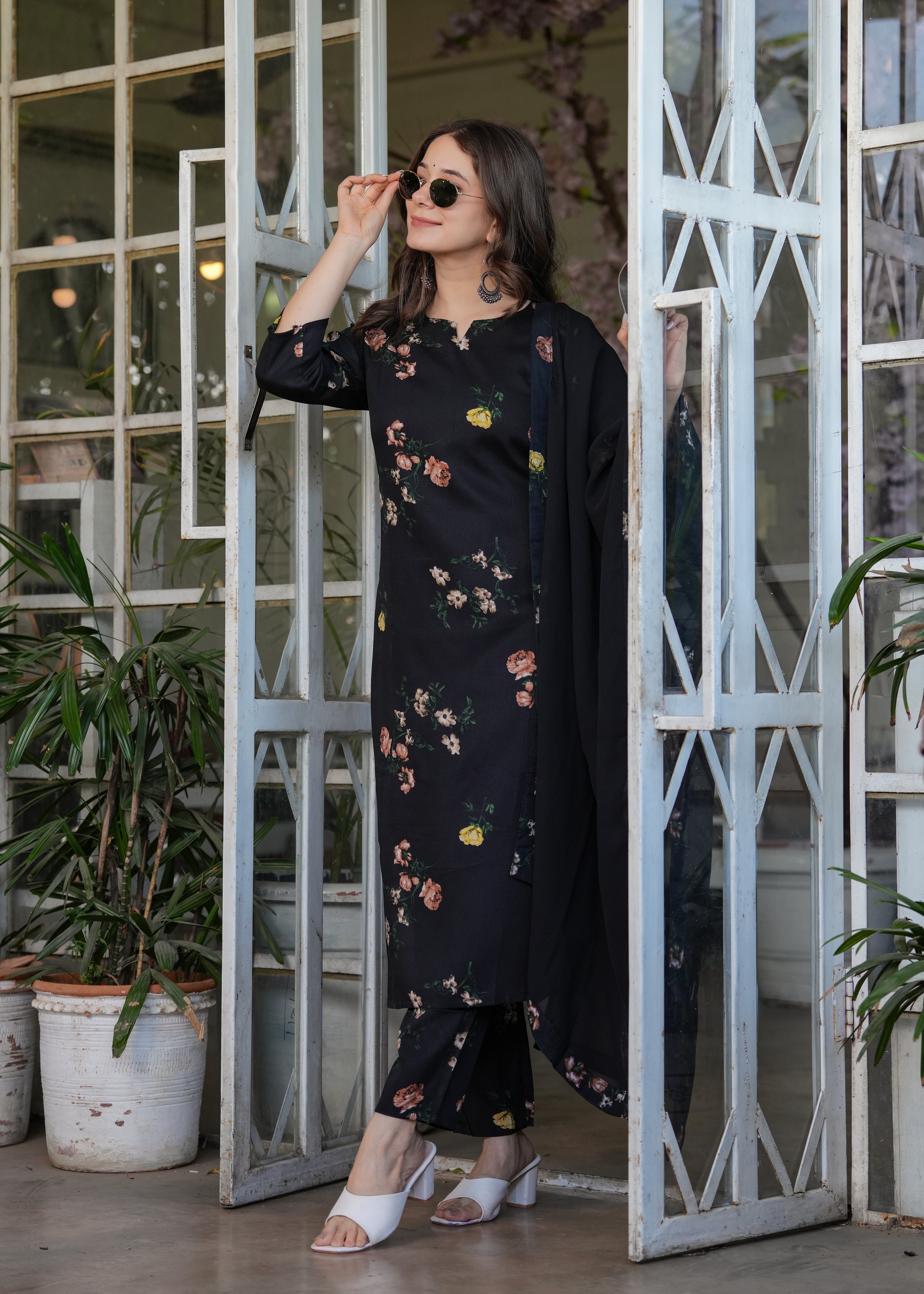 Woman adjusting her sunglasses while posing in the black silk blend floral printed kurta set, showing the kurti's length and sleeve detail.