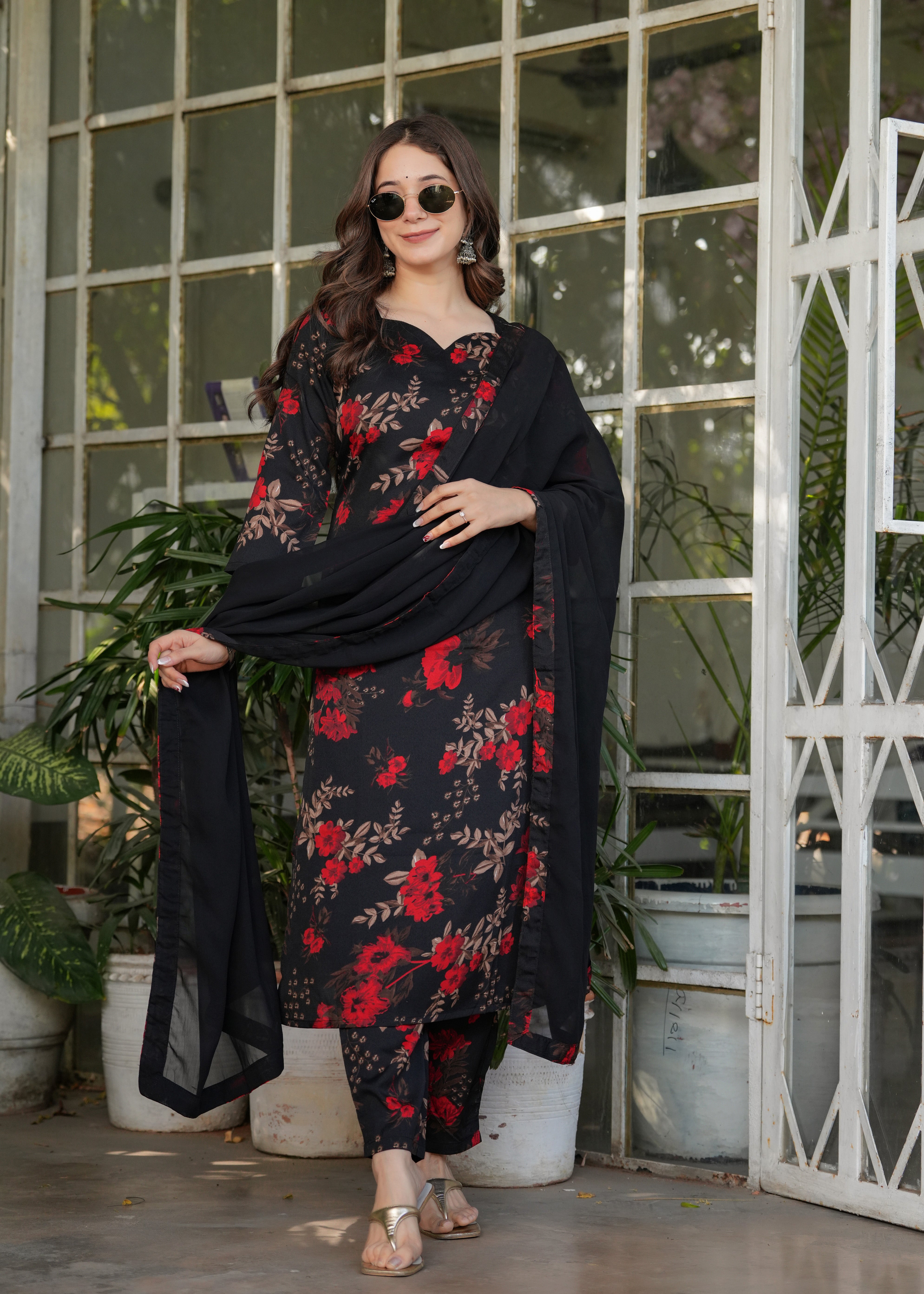 Woman in black printed kurta set with sunglasses, holding dupatta, stylish pose.