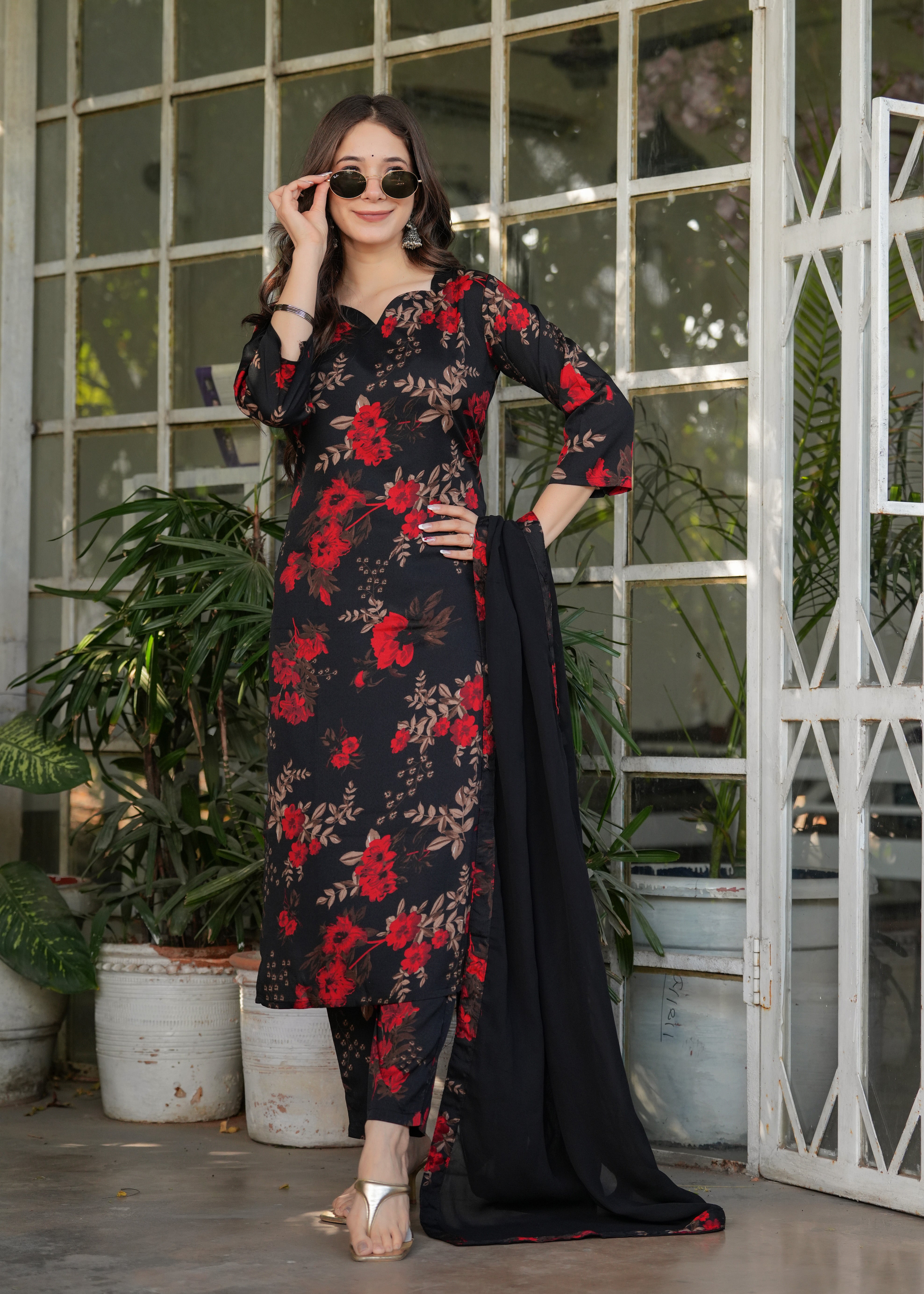 Woman adjusting sunglasses, showing black silk blend printed kurta with red flowers.
