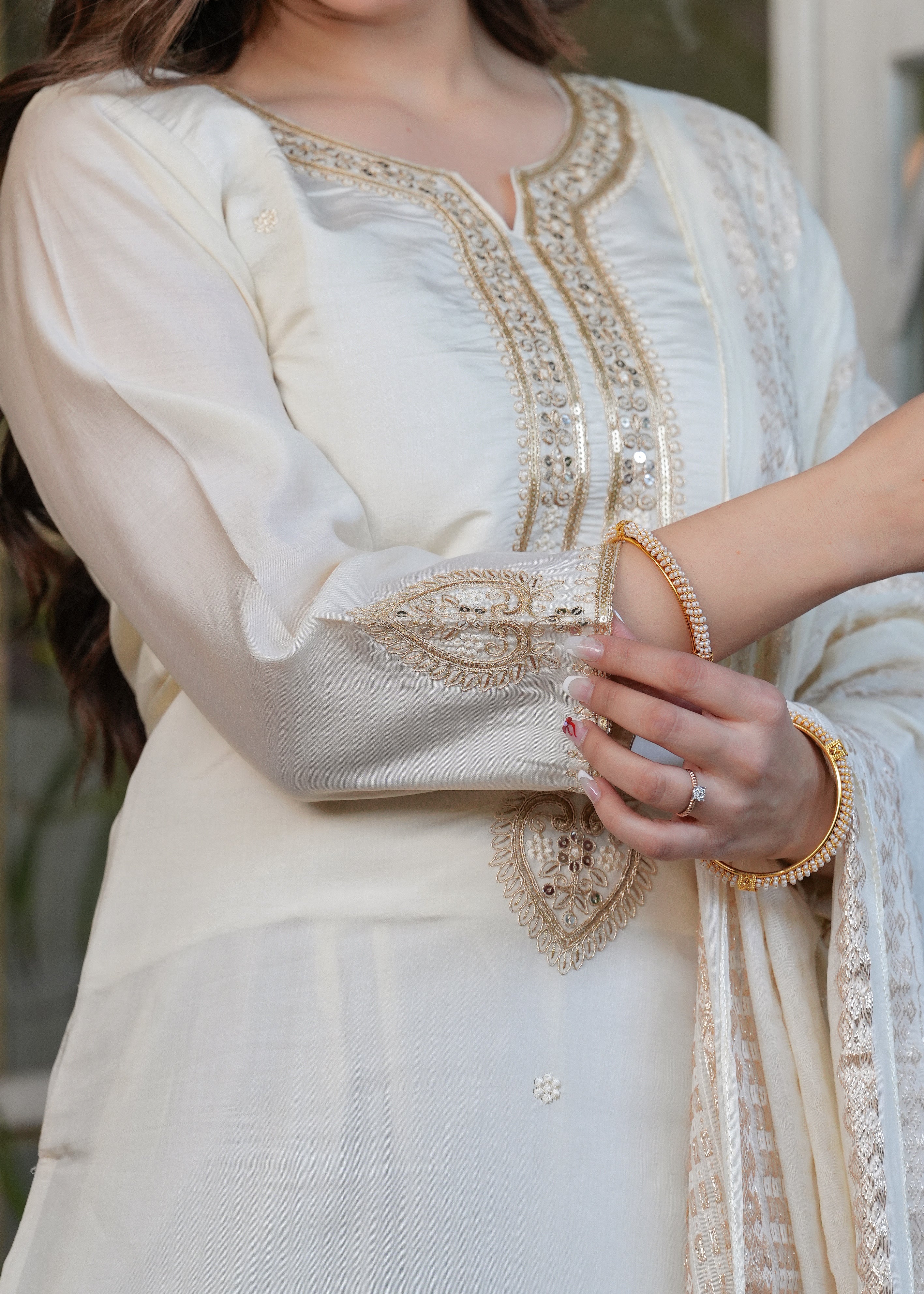 Detail shot of off-white kurta sleeve with embroidery and woman's hand with gold bangle