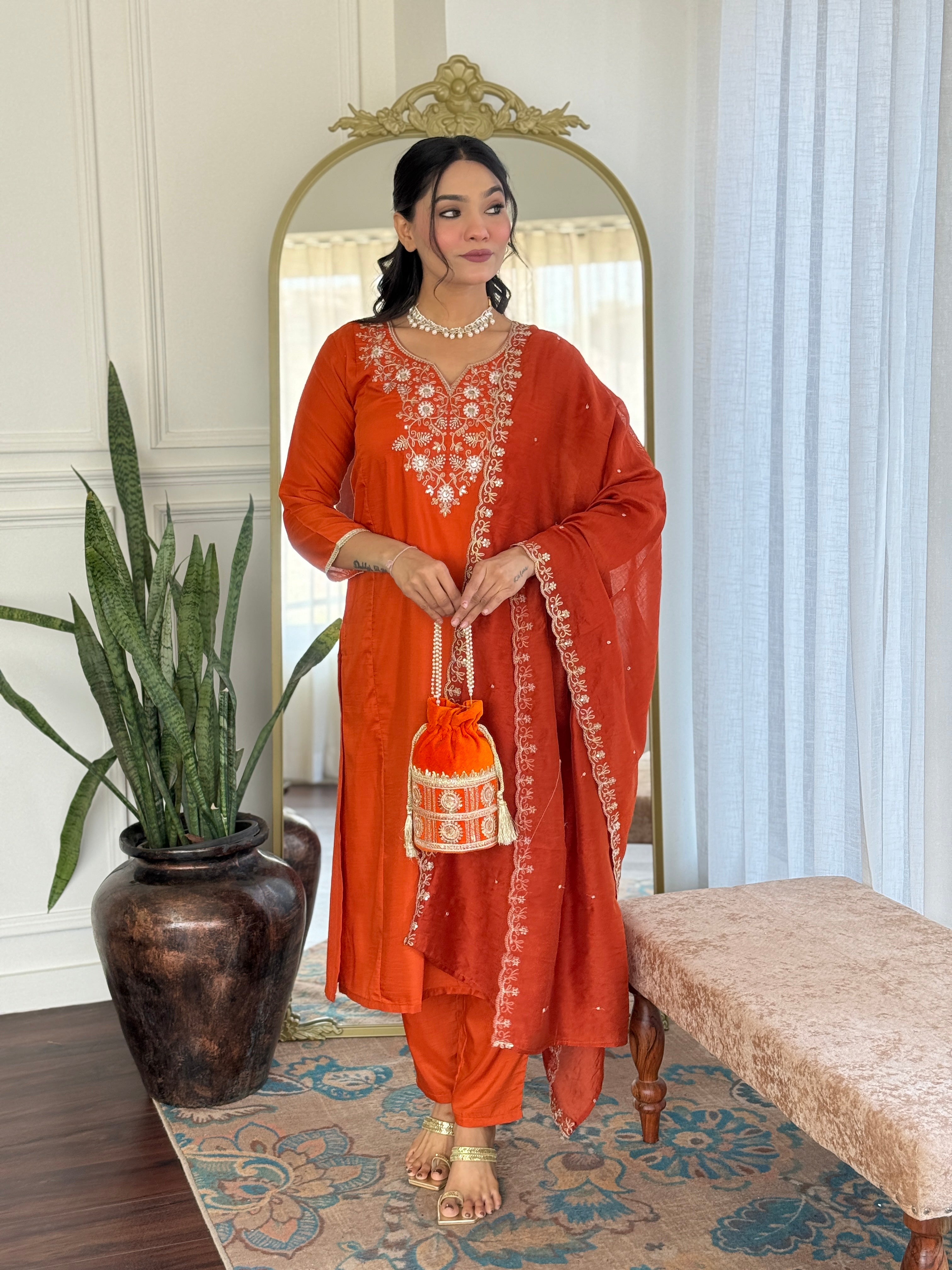 TRENDBUY model in elegant orange embroidered Viscose Chinon kurta set with matching dupatta, holding a potli bag, standing in a chic room.