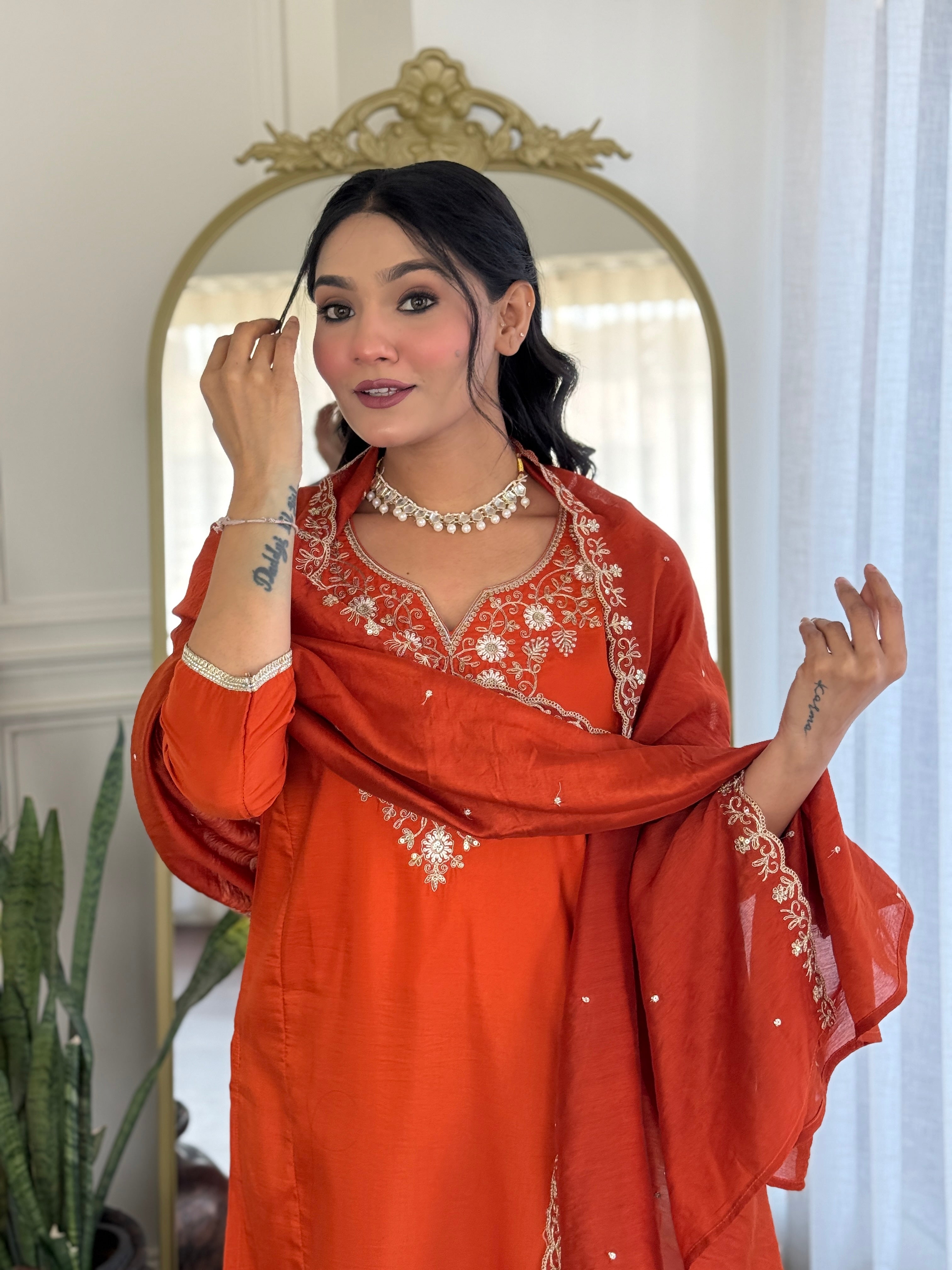 TRENDBUY model with a confident gaze, adjusting her hair, wearing the orange embroidered kurta set with a matching dupatta.