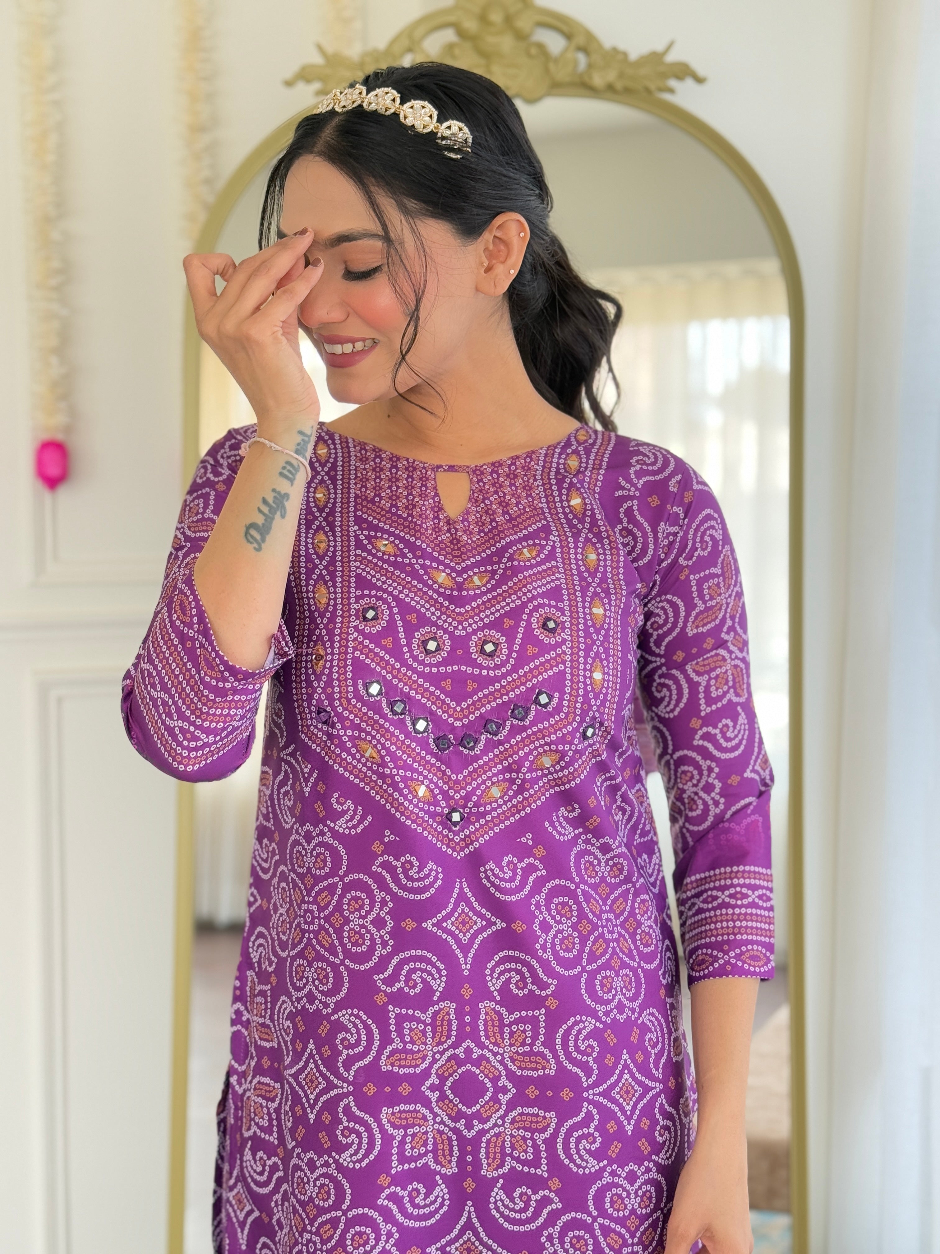 Smiling model, highlighting the beauty of the hand mirror work and the rich purple fabric of the ethnic wear.