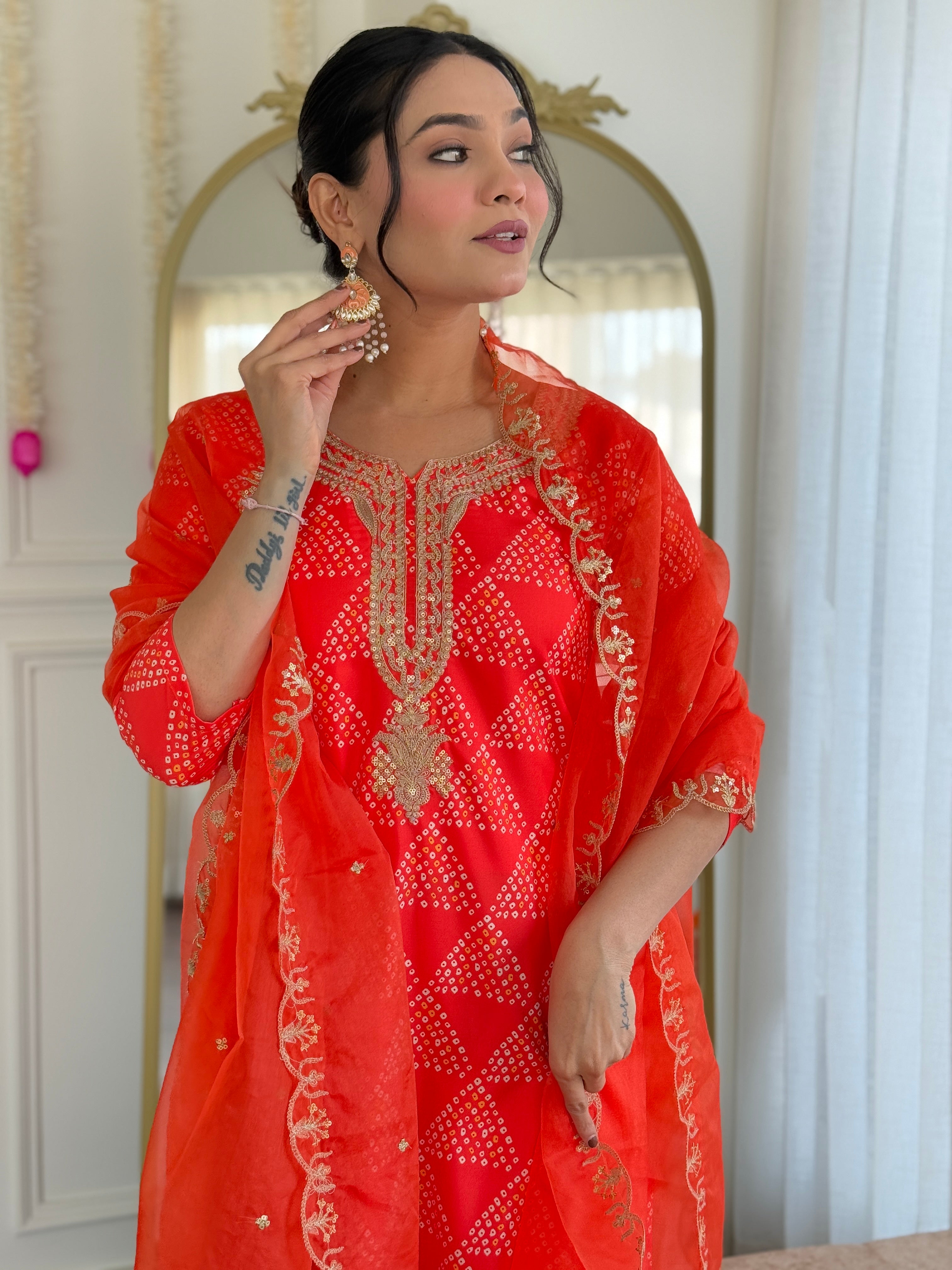 Woman gracefully adjusting her orange organza dupatta, emphasizing the detailed embroidery on the kurti and dupatta border.