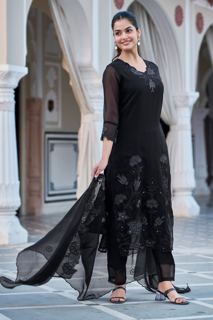 Side profile of a woman in a black georgette kurti set, gracefully twirling the dupatta to display its beautiful drape and border embroidery.