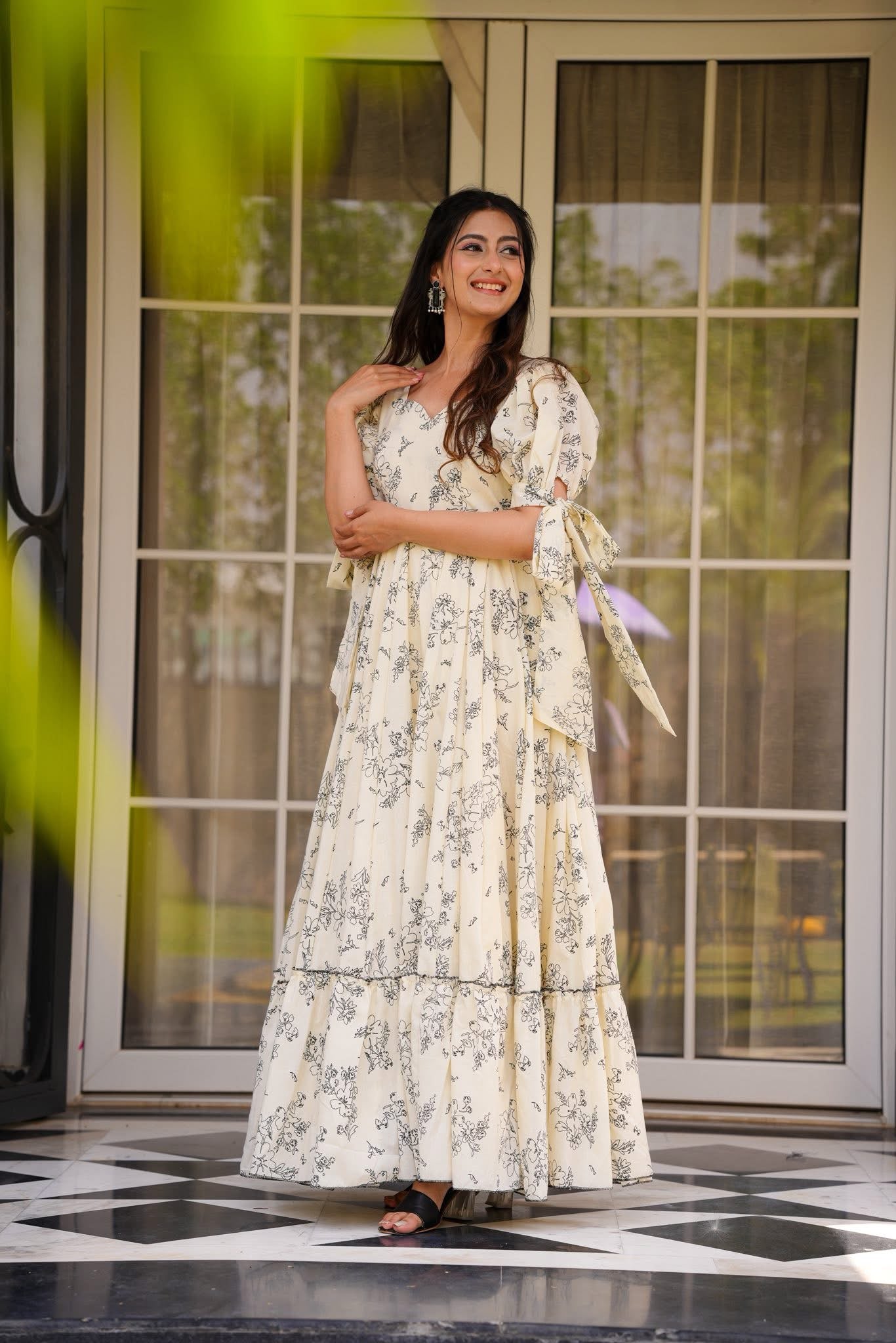 Elegant woman with hand on chest, posing in a cream floral print maxi dress, highlighting the silhouette