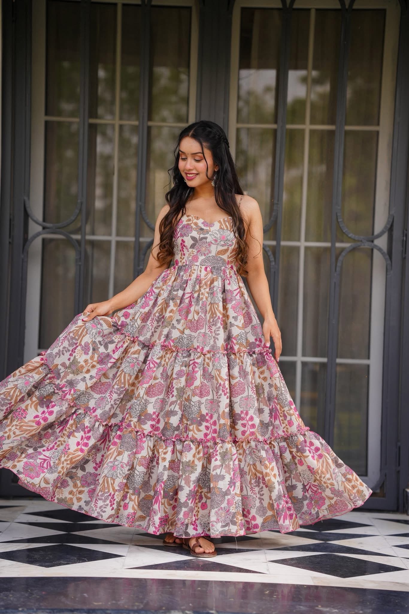 Full shot of a smiling woman twirling in a white and pink tiered floral print Western maxi dress with spaghetti straps.