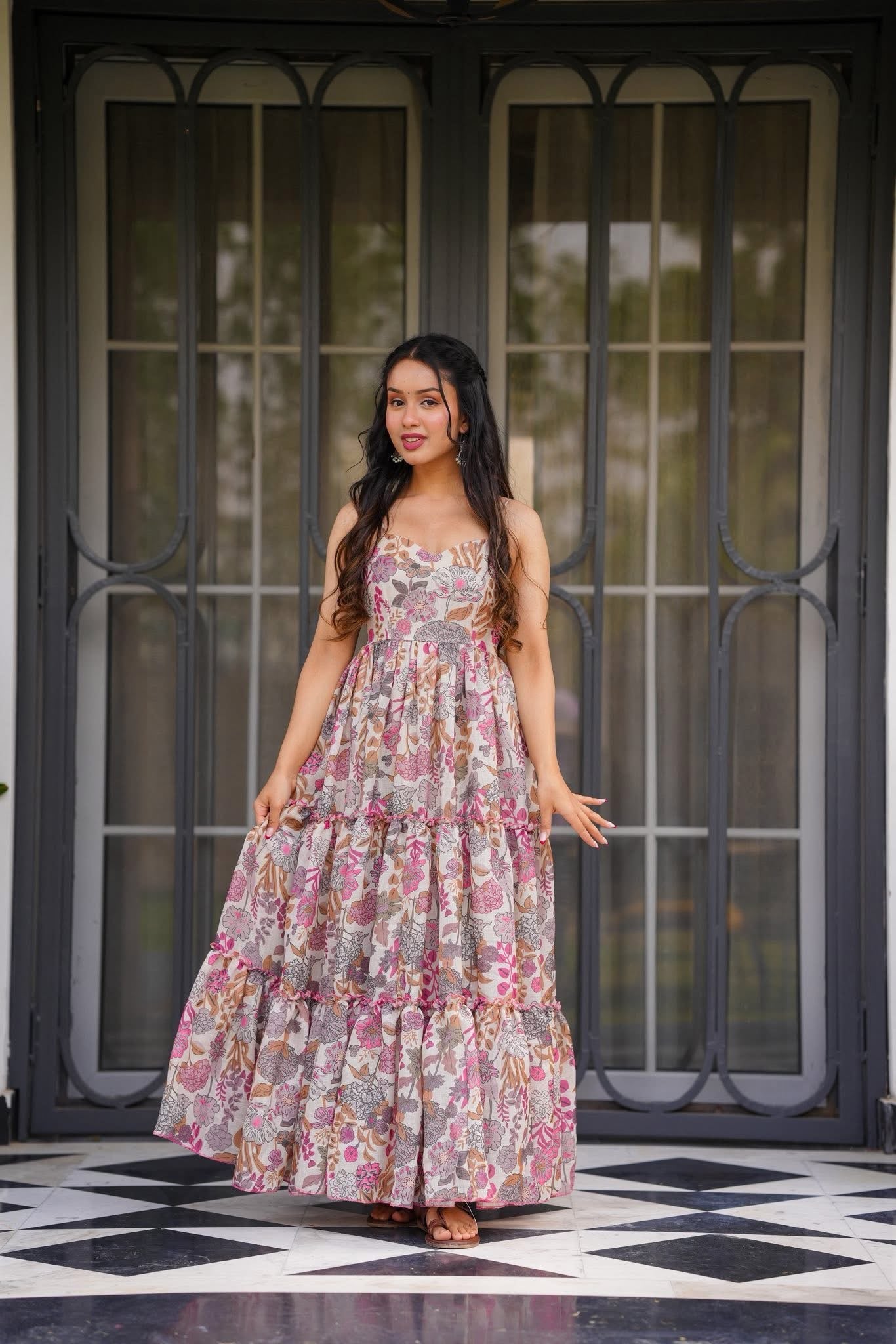 Attractive woman posing front-facing in a long, flowing floral print tiered maxi dress with thin straps.