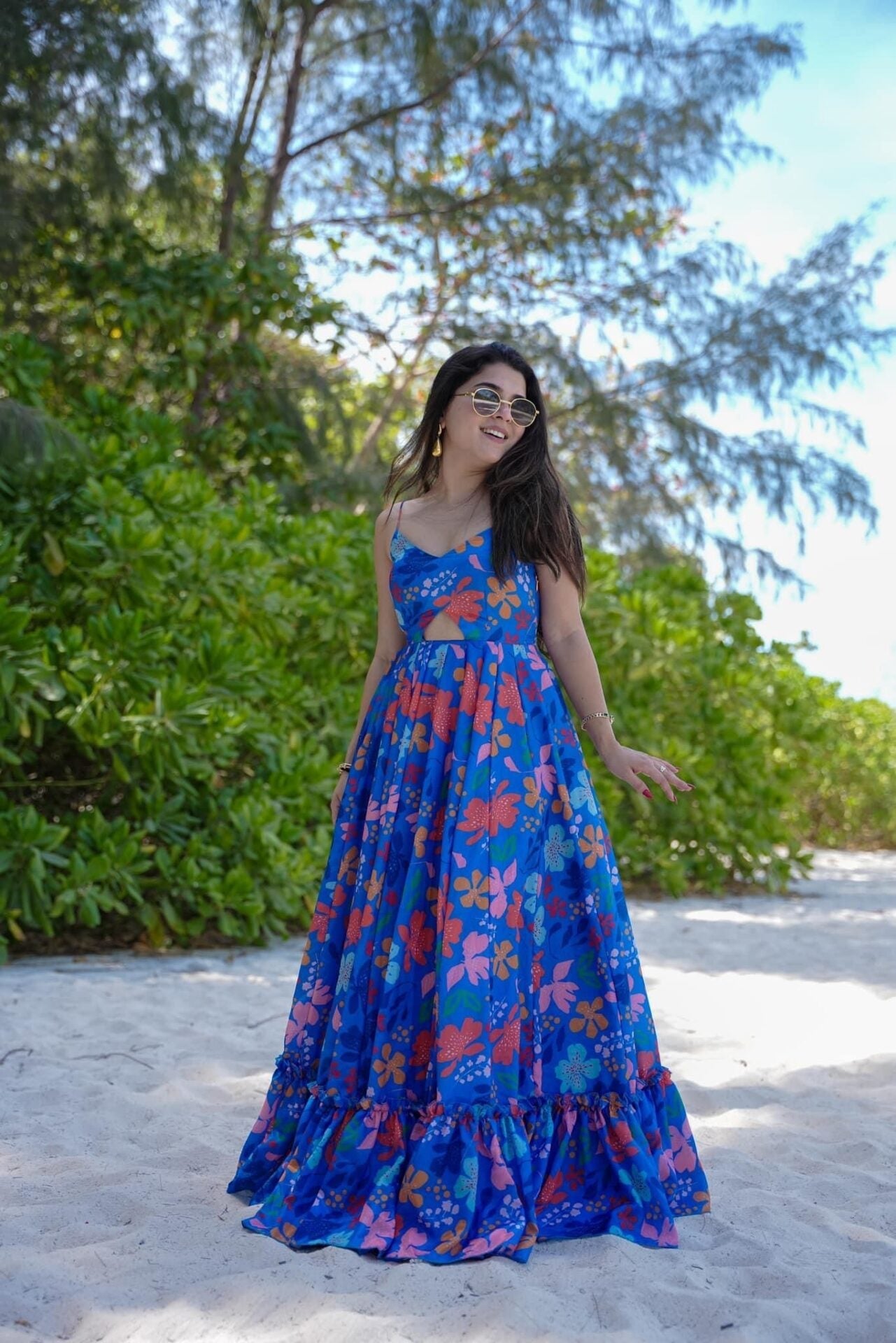 TRENDBUY model in vibrant blue floral poly rayon maxi dress with spaghetti straps and midriff cut-out, posing happily on a sunny beach path.