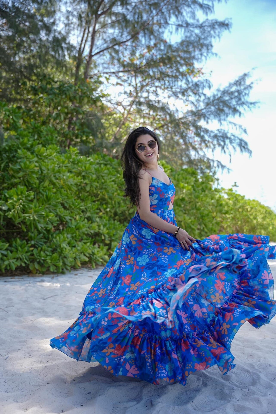 TRENDBUY model gracefully spinning, showcasing the flowing fabric and playful design of her blue floral maxi dress on a sandy beach.