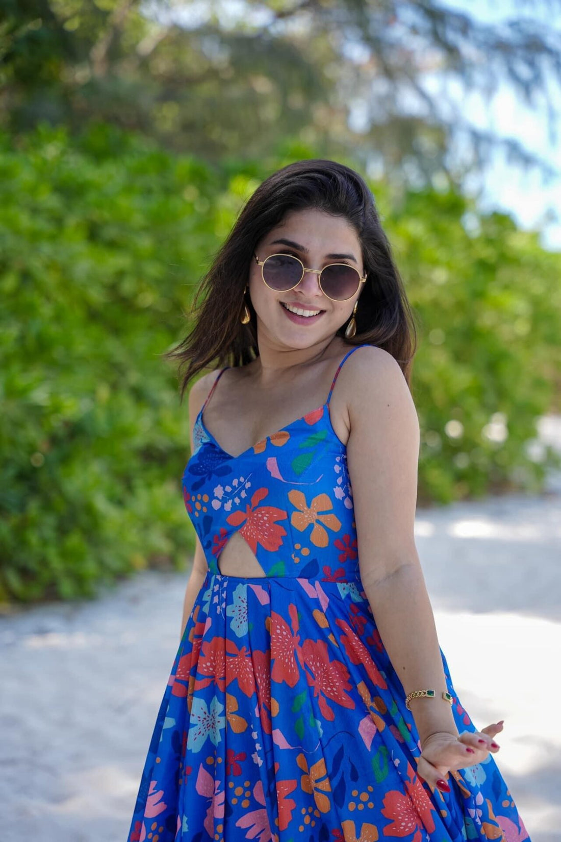 Close-up of TRENDBUY model smiling in a stylish blue floral spaghetti strap dress with a subtle cut-out, wearing chic round sunglasses.