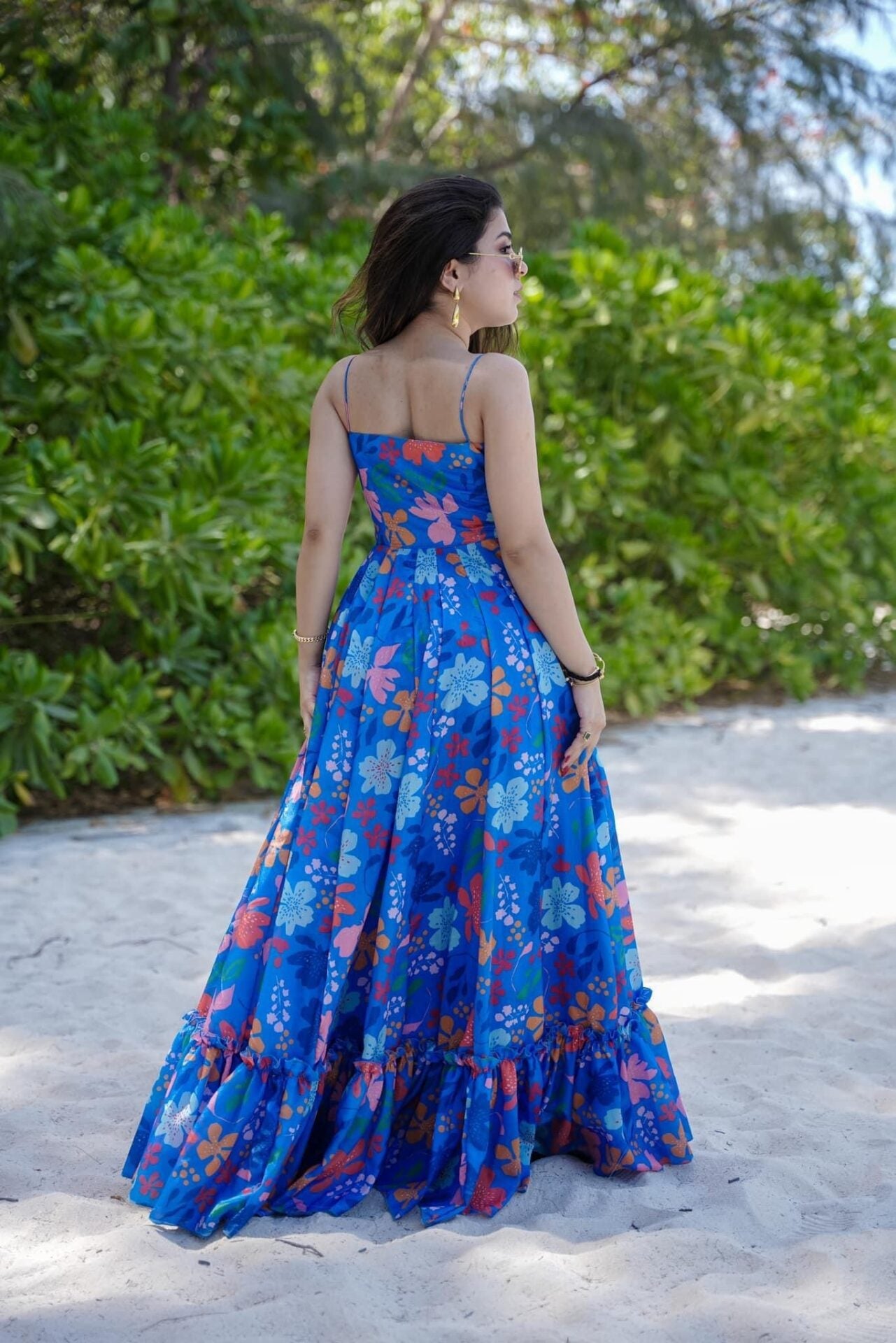 Back view of TRENDBUY model walking away on a beach path, highlighting the elegant drape and ruffled hem of the blue floral print maxi dress.
