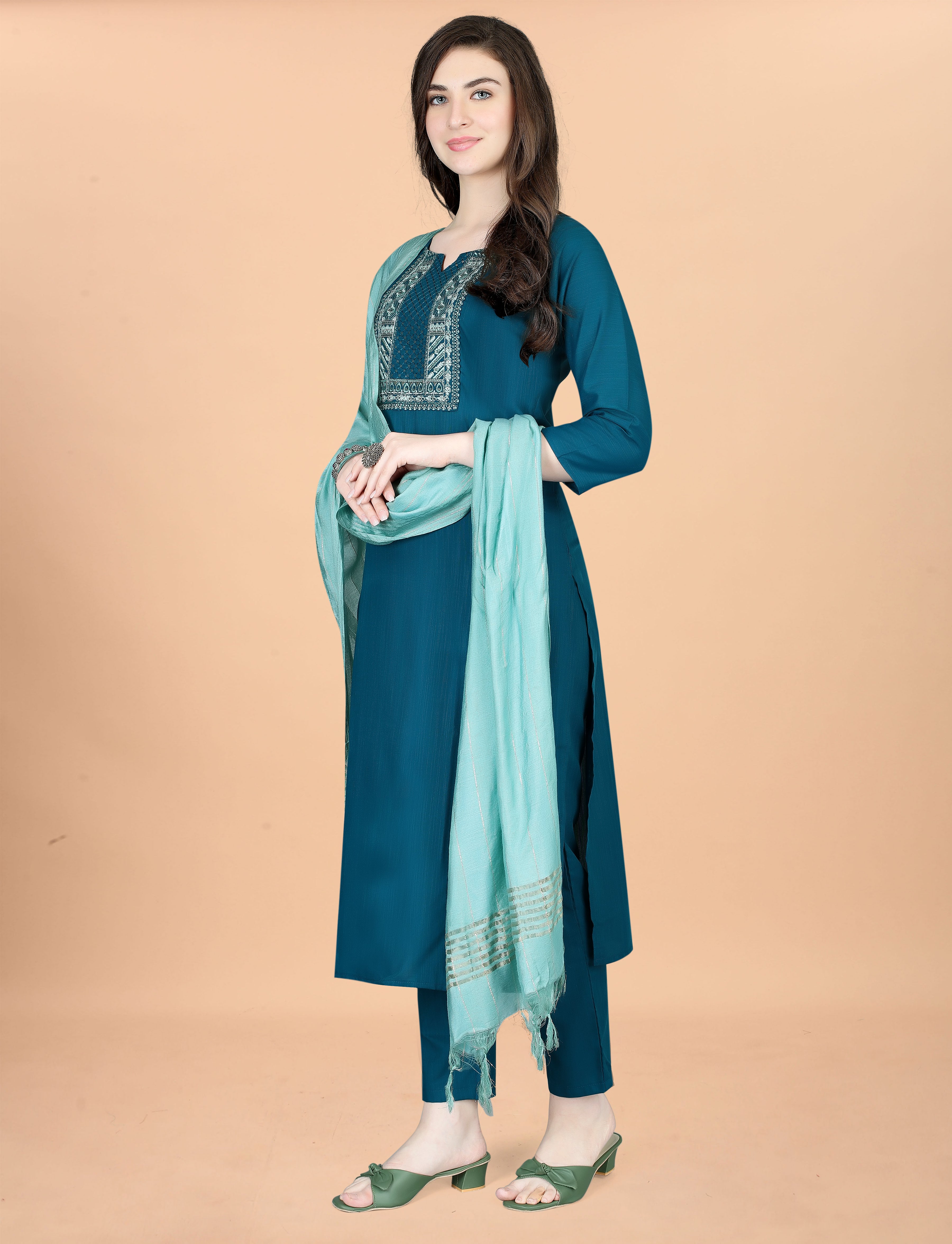Side profile of a woman posing in a teal embroidered kurti set, emphasizing the outfit's elegant silhouette and the drape of the mint green chanderi dupatta.