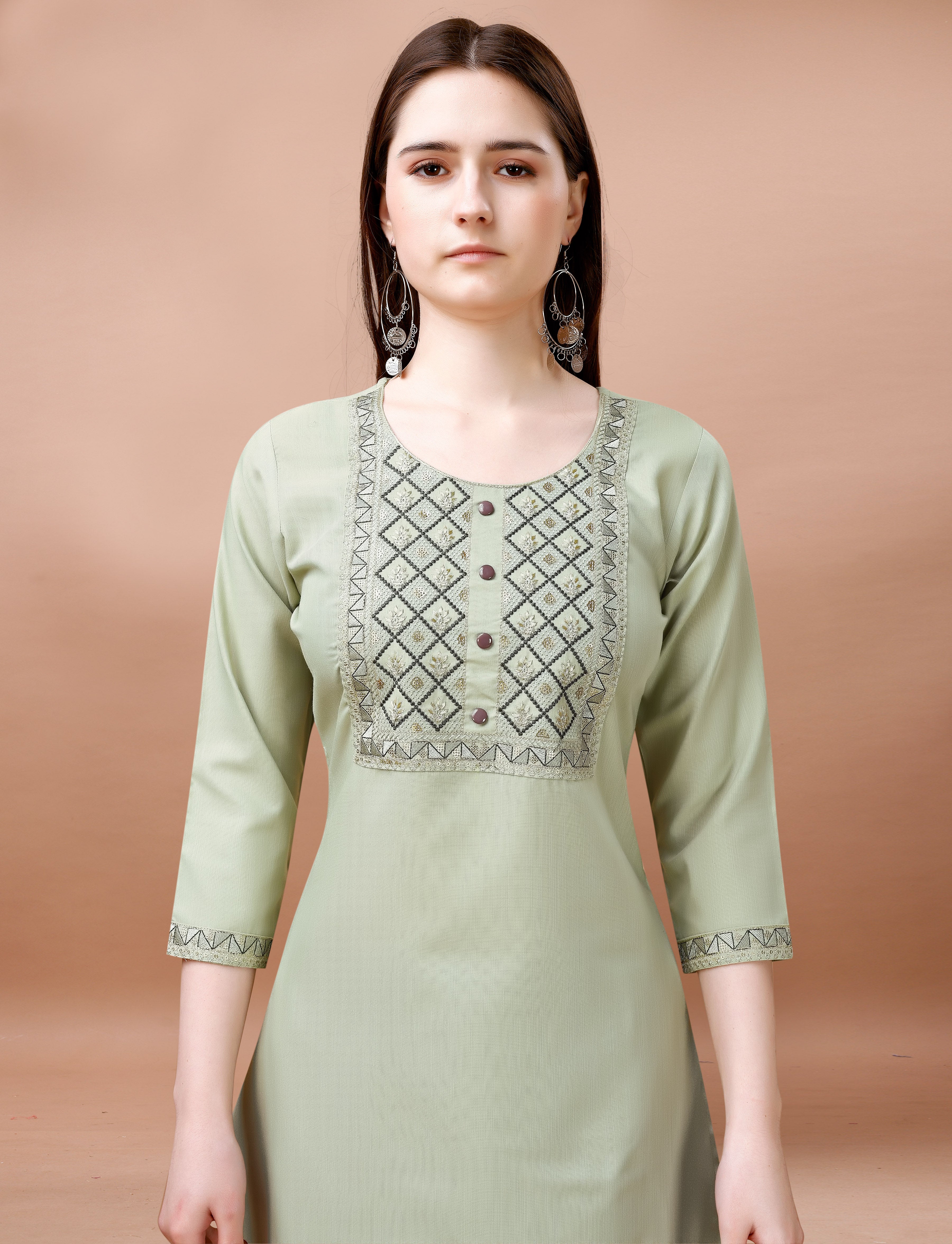 Close-up of a woman's upper body, highlighting the elaborate geometric embroidery on the neckline and sleeves of a sage green cotton blend kurti.