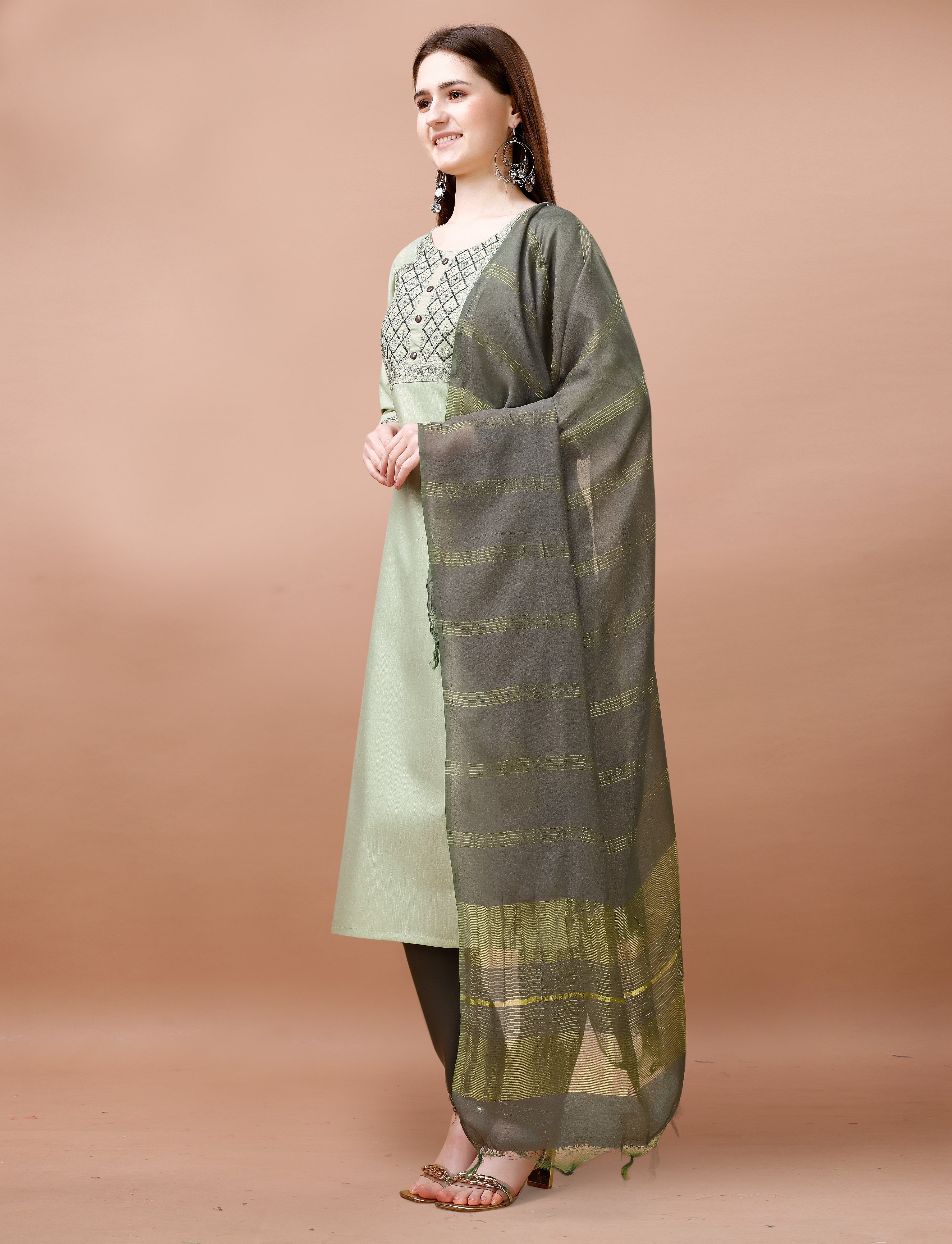 Full-length view of a woman in a sage green embroidered kurta set with charcoal grey pants and dupatta, holding a clutch.